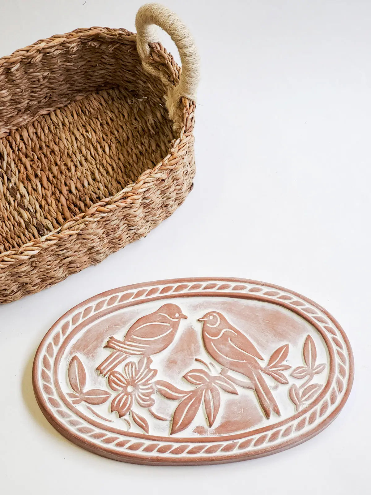 Woven seagrass basket with rope handle beside ceramic bird plaque, farmhouse decor