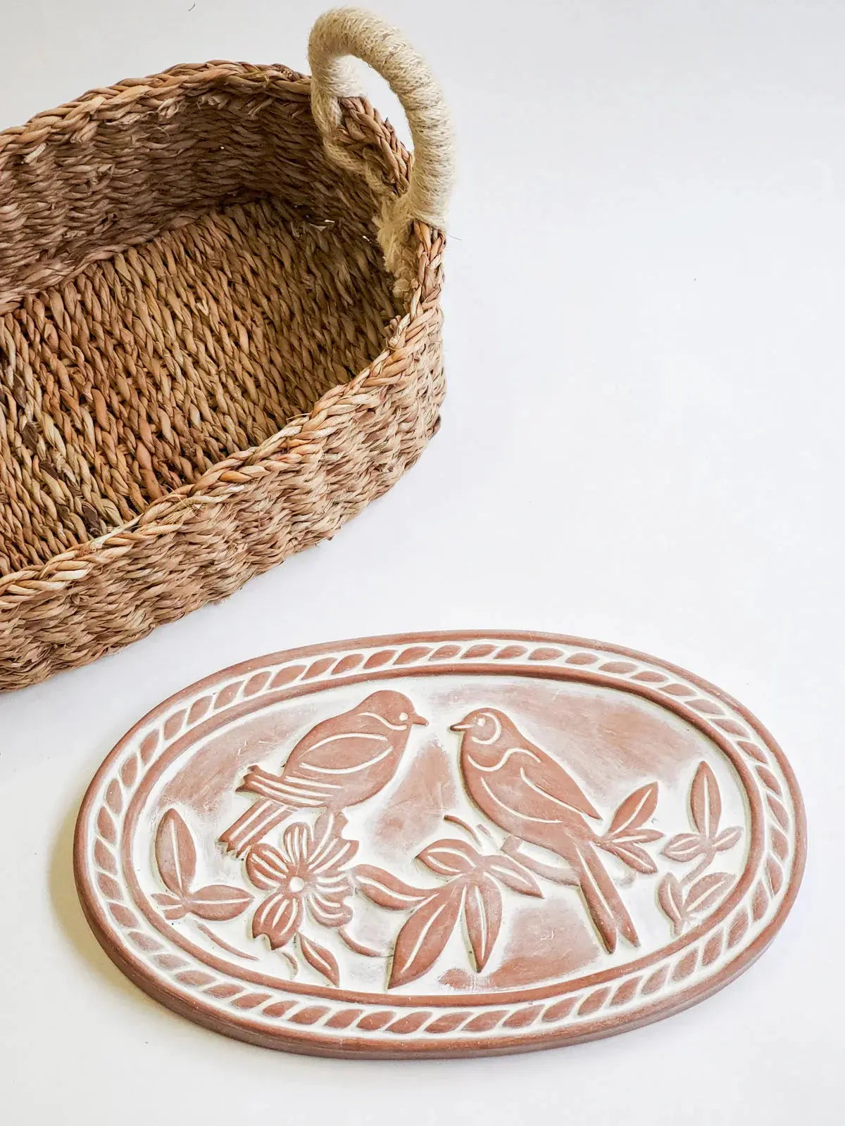Woven seagrass basket with rope handle beside ceramic tray featuring embossed birds and floral design, farmhouse decor