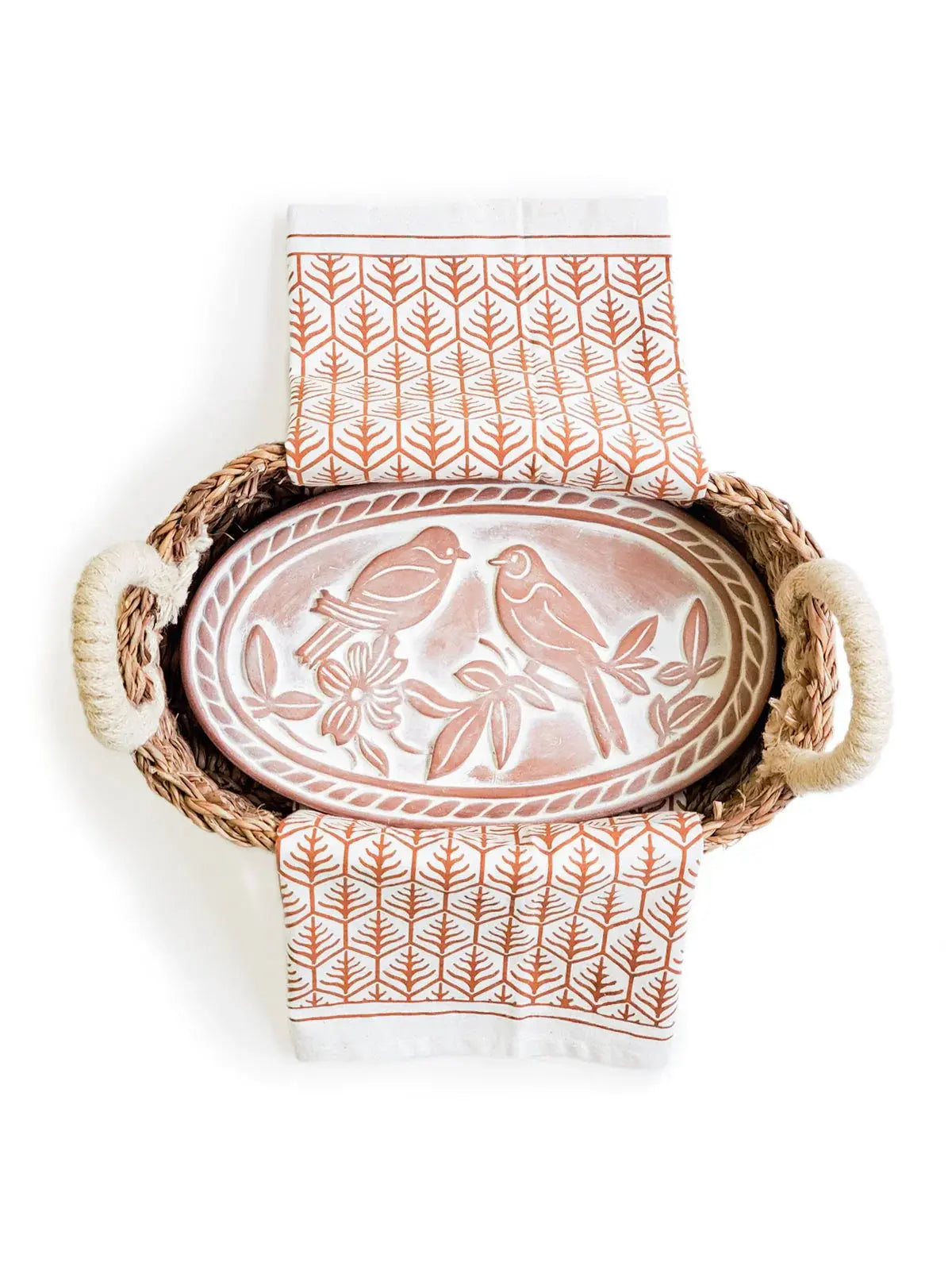 Farmhouse-style wicker basket with bird-patterned ceramic tray and leaf-print kitchen towels