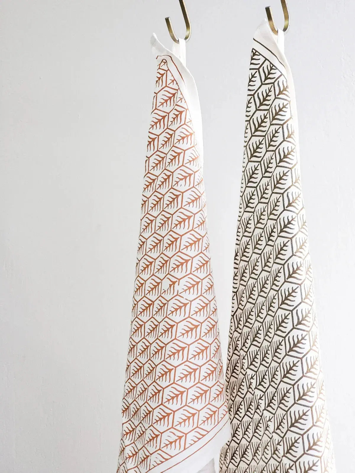 Farmhouse kitchen towels with leaf print, hanging on brass hooks for cozy cottage decor