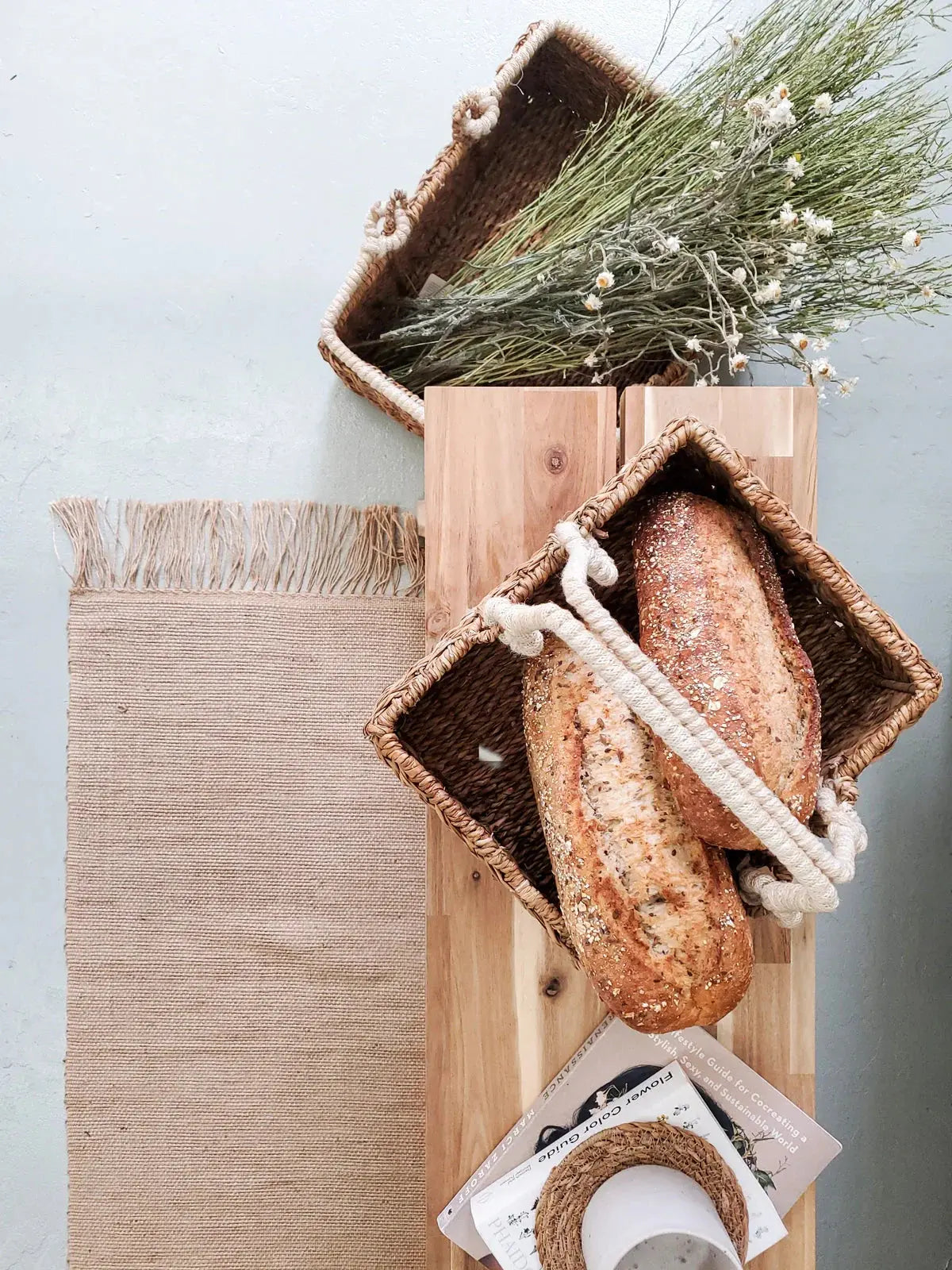 Woven basket with fresh bread, dried flowers, and rustic home decor on wooden board