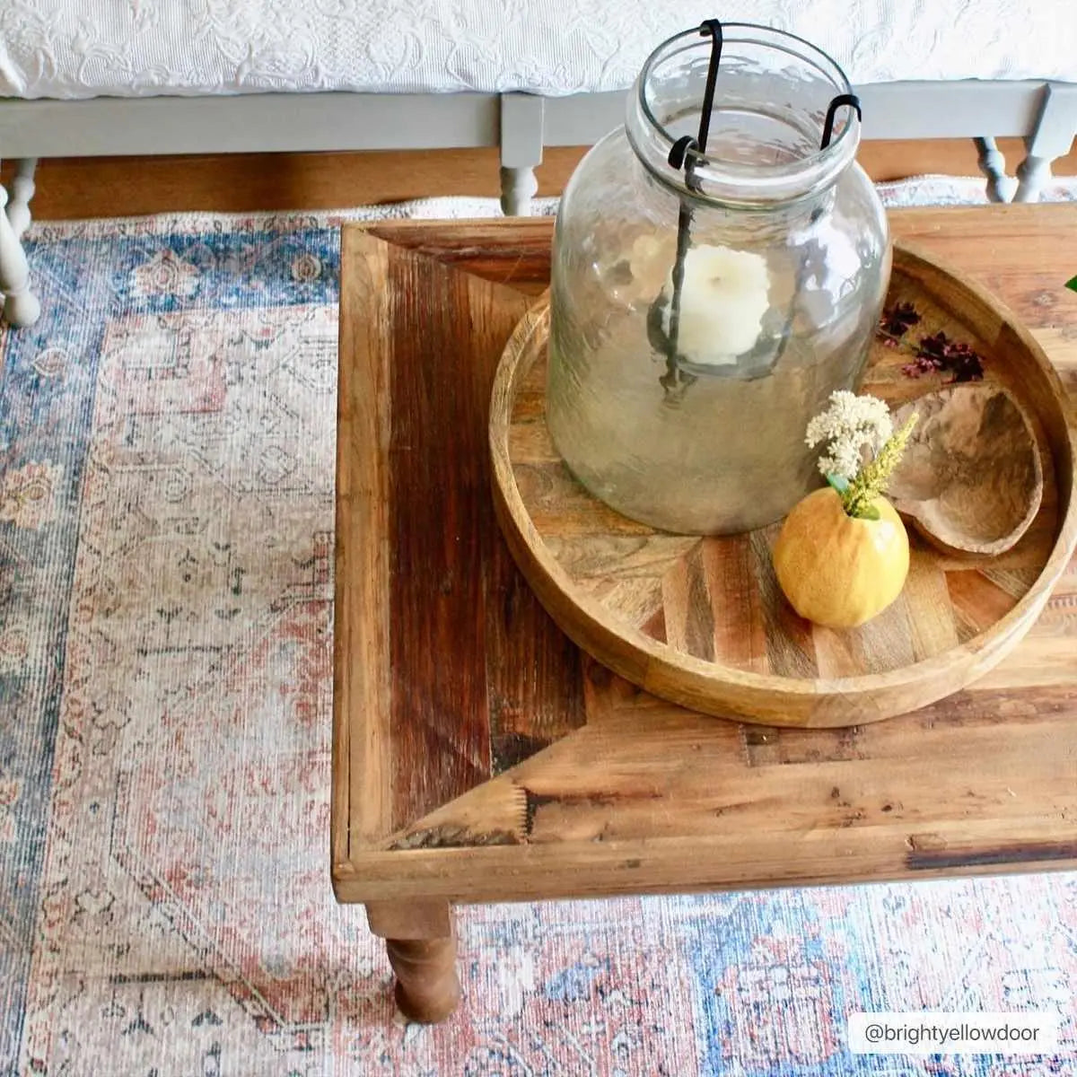 Rustic wood tray with glass candle holder, mini pumpkin, and dried flowers on farmhouse coffee table