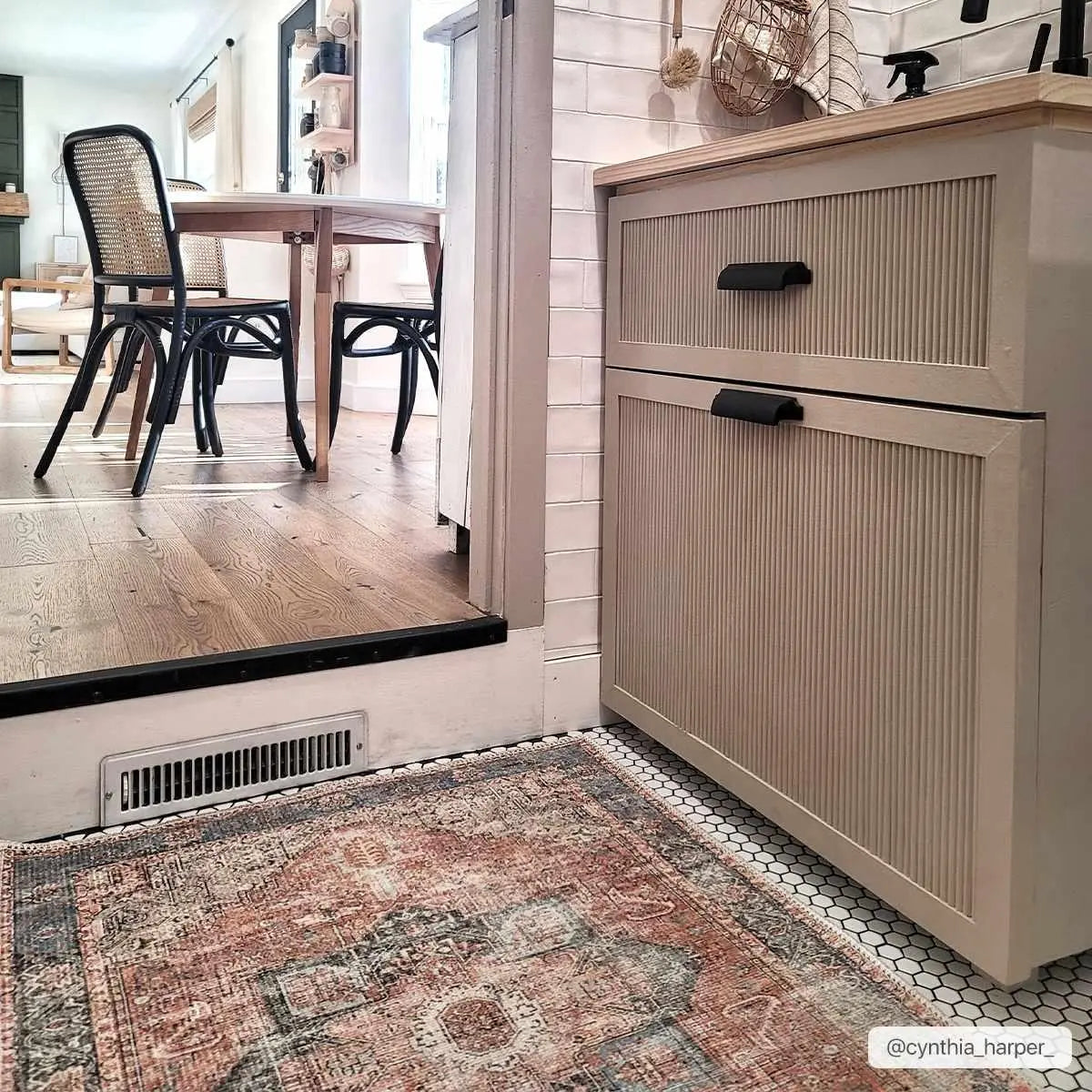 Beige farmhouse cabinet with black handles, vintage rug, and dining area in cozy cottage-style home
