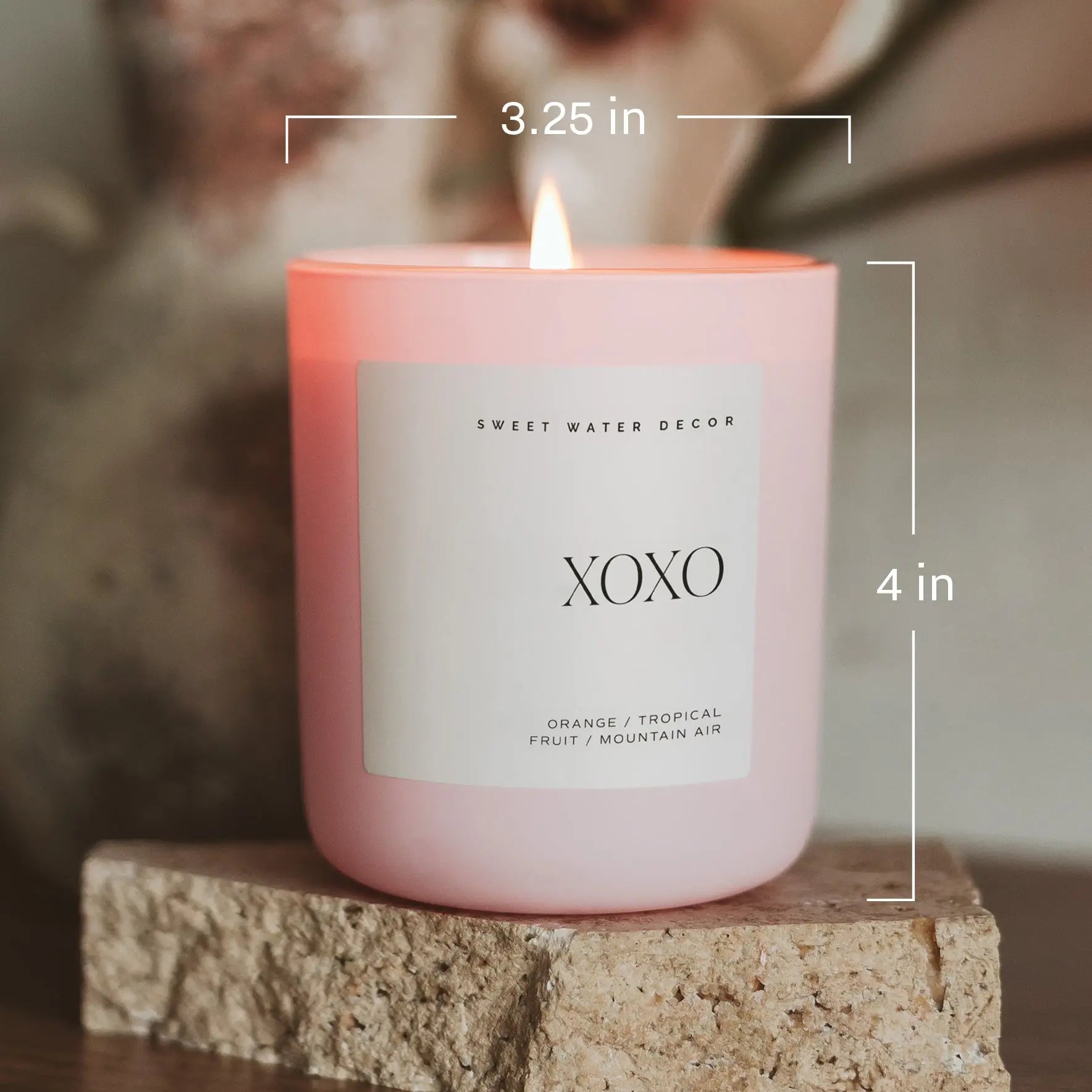 Pink candle labeled 'XOXO' with measurements on a stone surface