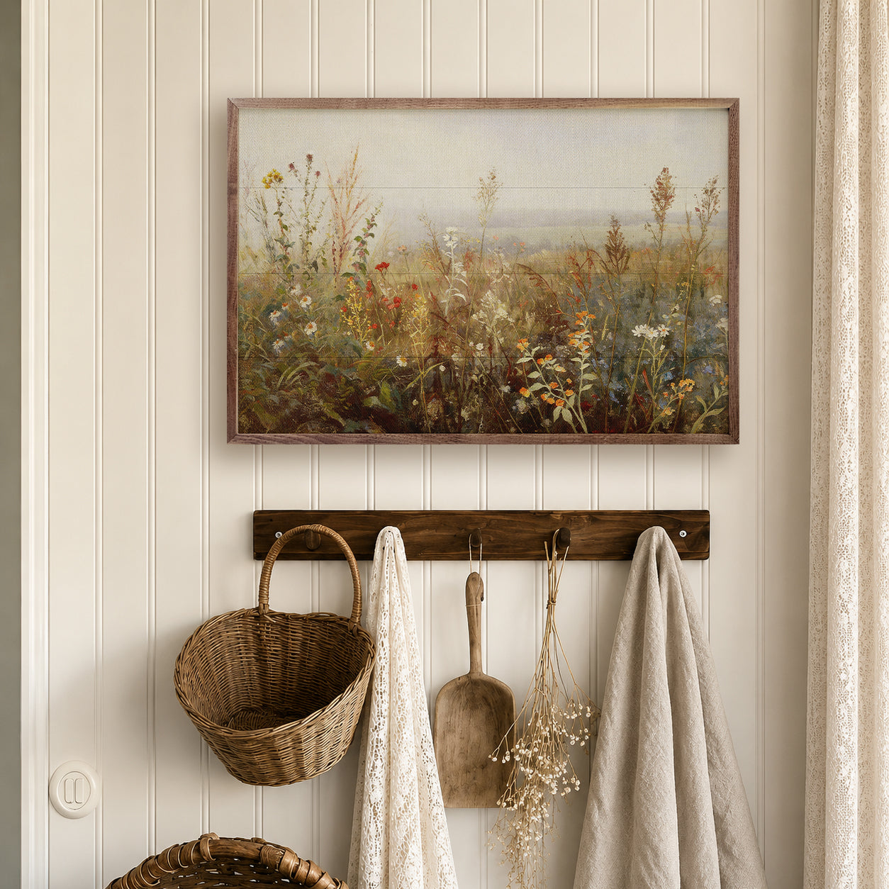 Decorative wall with framed artwork of a field, hooks with a basket, towel, and plant, against a light wooden panel background.