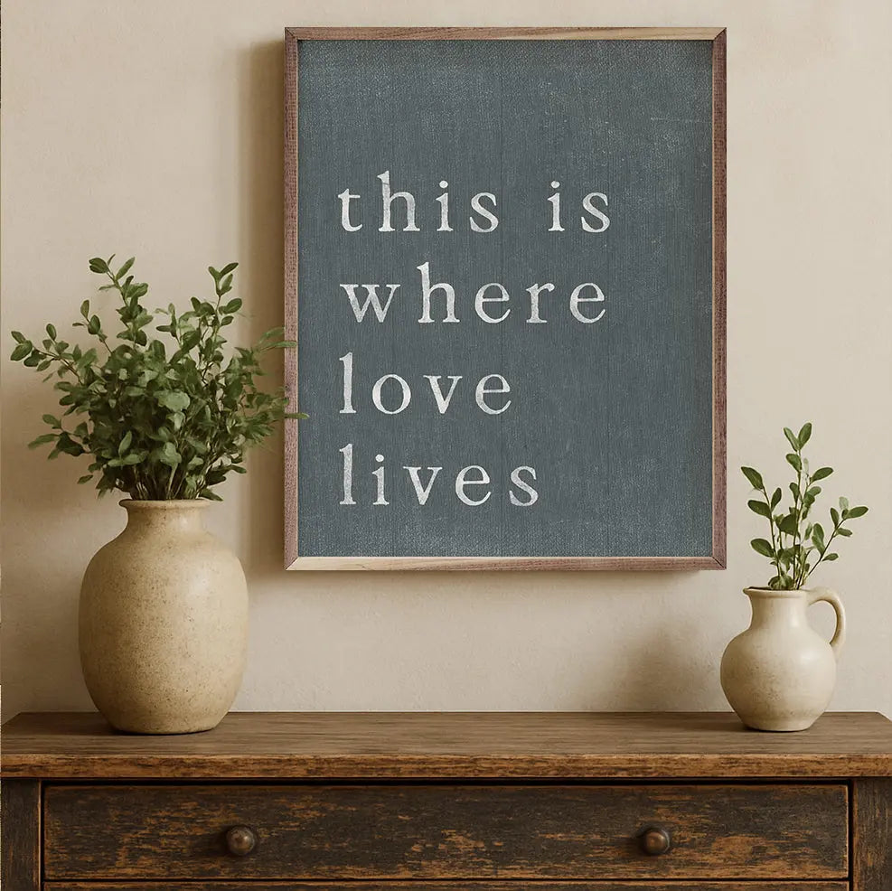 Chalkboard with text "this is where love lives" on beige wall wih two beige pots on a wooden table