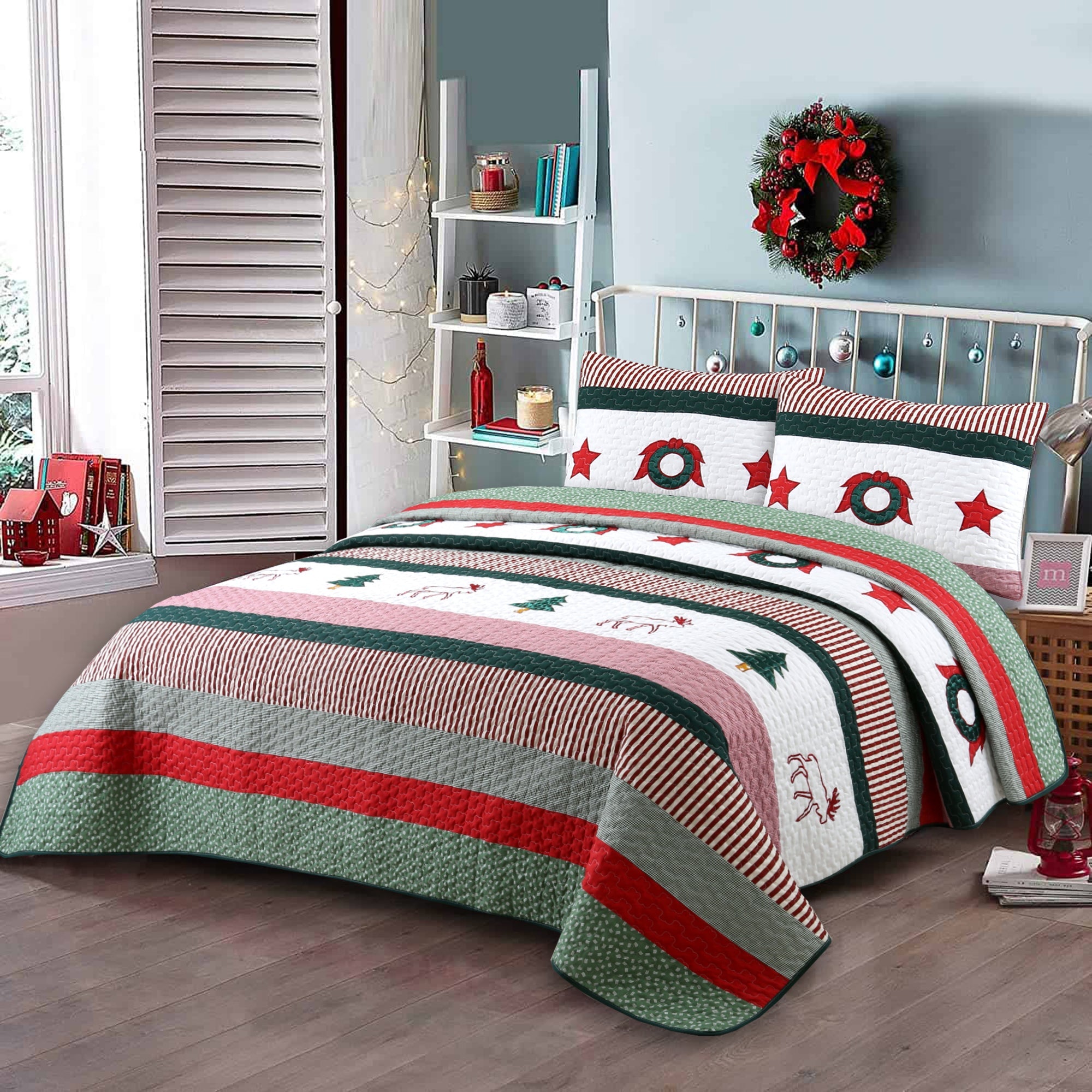 A Christmas-themed quilted bedding set with matching pillowcases, featuring stripes and motifs of green wreaths, red stars, and 'Merry Christmas' text on a white background, styled in a bedroom setting.