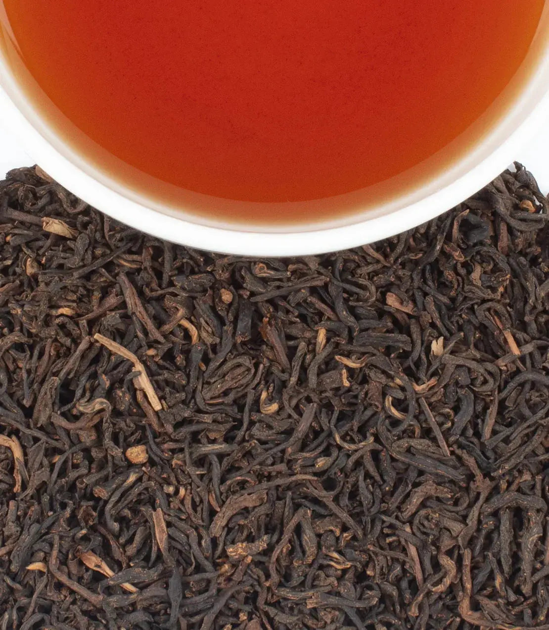 Rich amber tea in white cup surrounded by loose black tea leaves, cozy farmhouse style