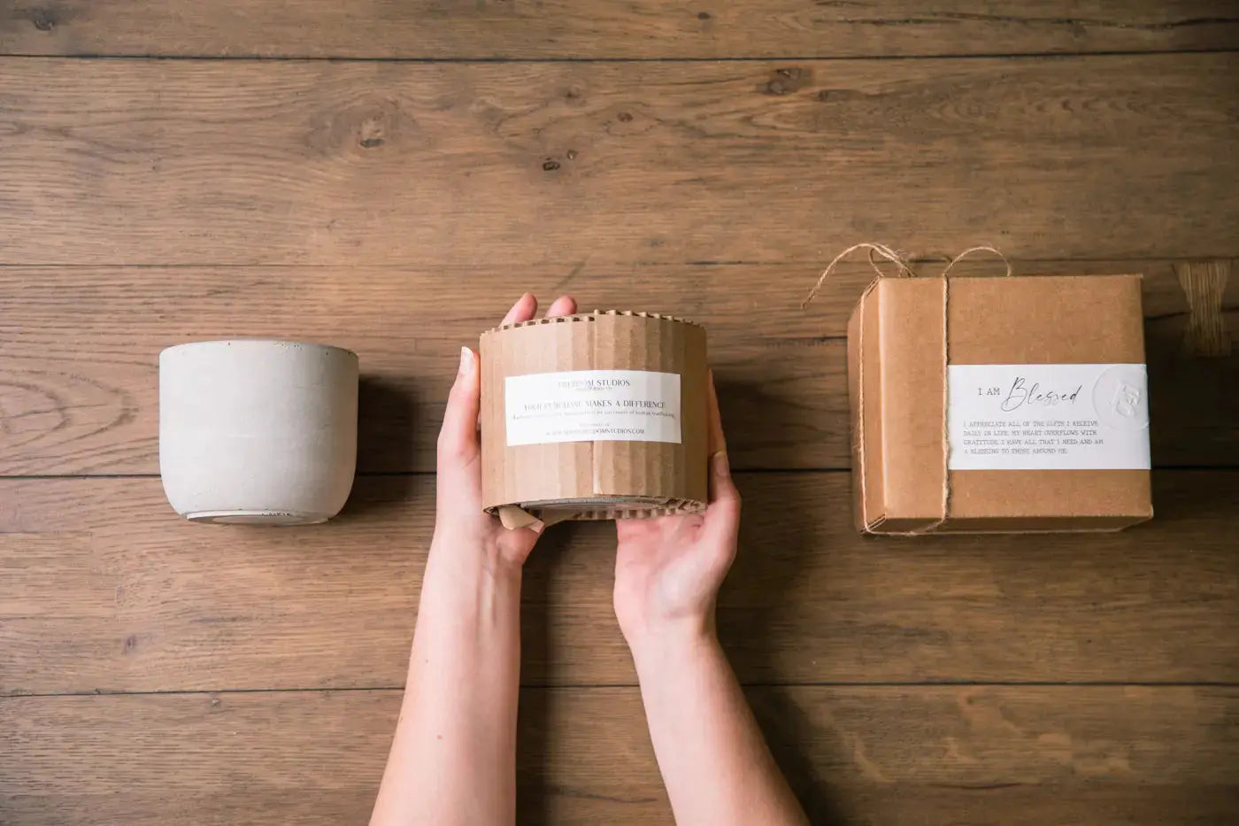 Person holding a cylindrical product with a label, next to a similar product and packaging on a wooden surface.