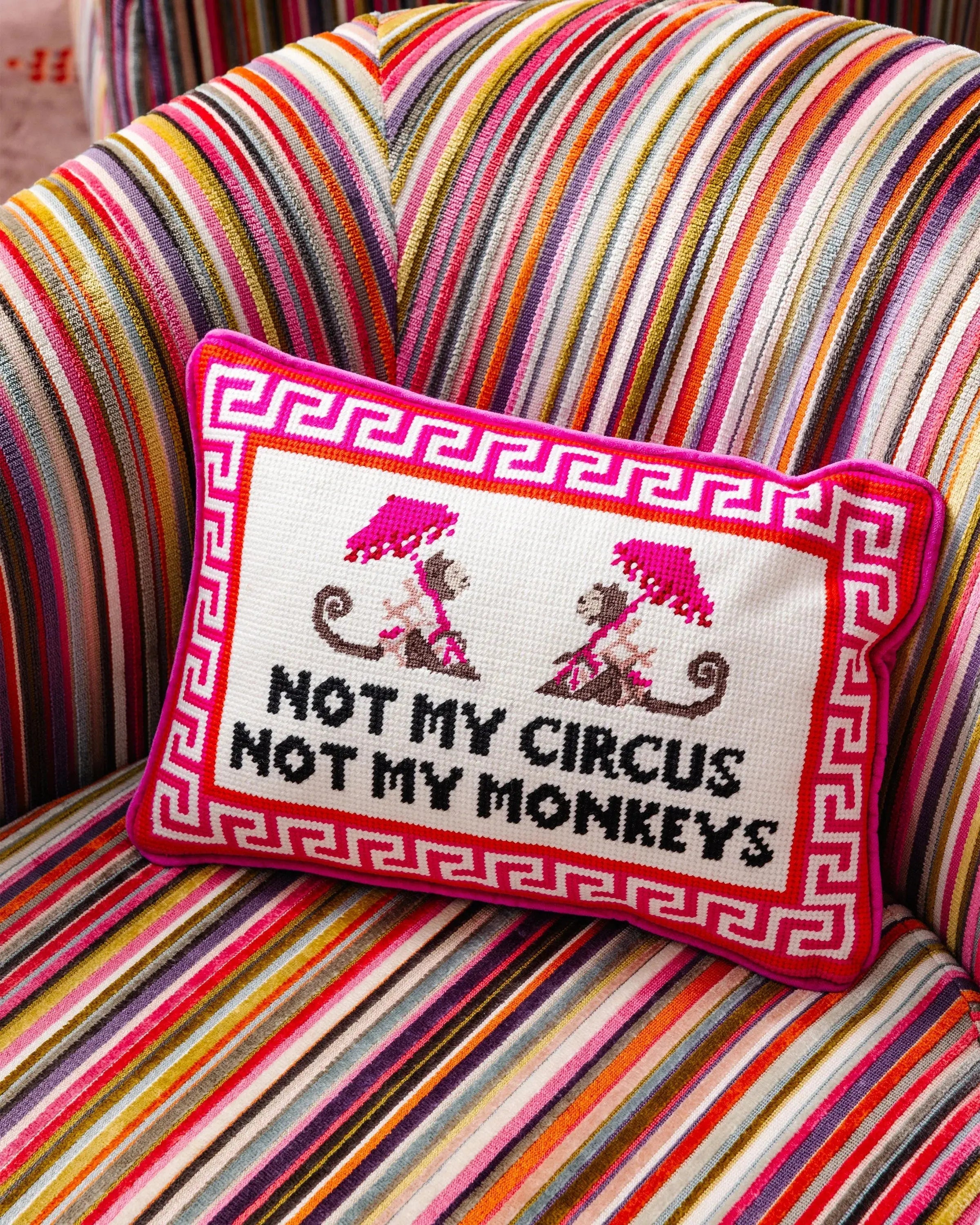 Funny needlepoint pillow with 'Not My Circus Not My Monkeys' quote on colorful striped armchair, cozy home decor