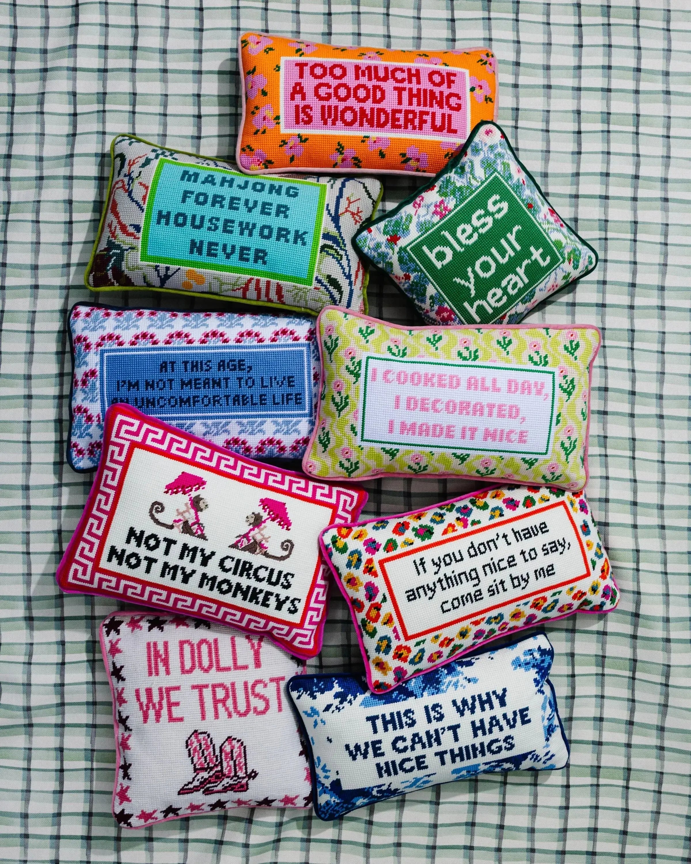 Colorful embroidered quote pillows with funny sayings, perfect for cozy farmhouse or cottage decor on a plaid background.