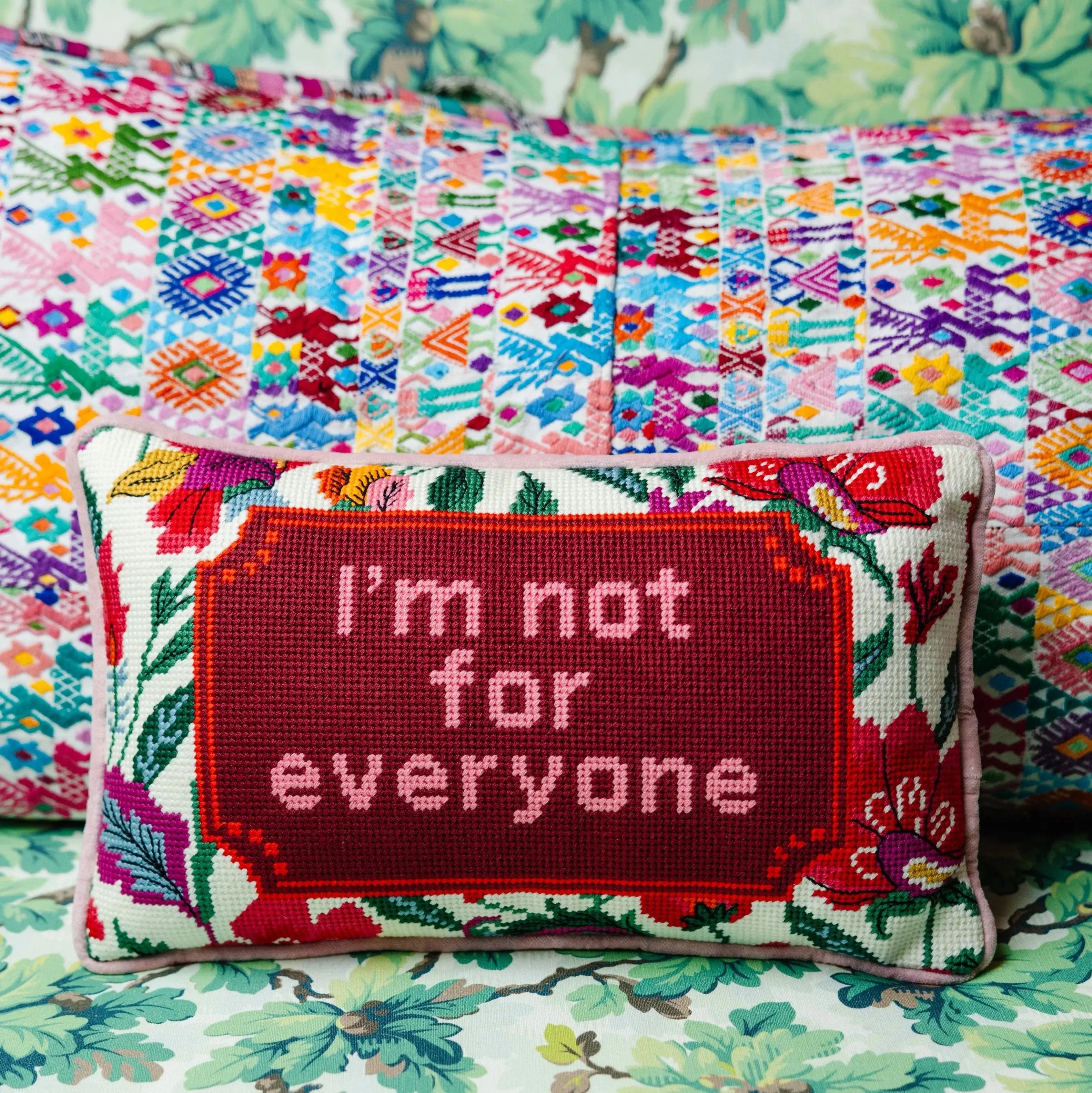 Cross-stitch pillow with 'I'm not for everyone' quote, floral border, on colorful quilted background, cozy farmhouse decor