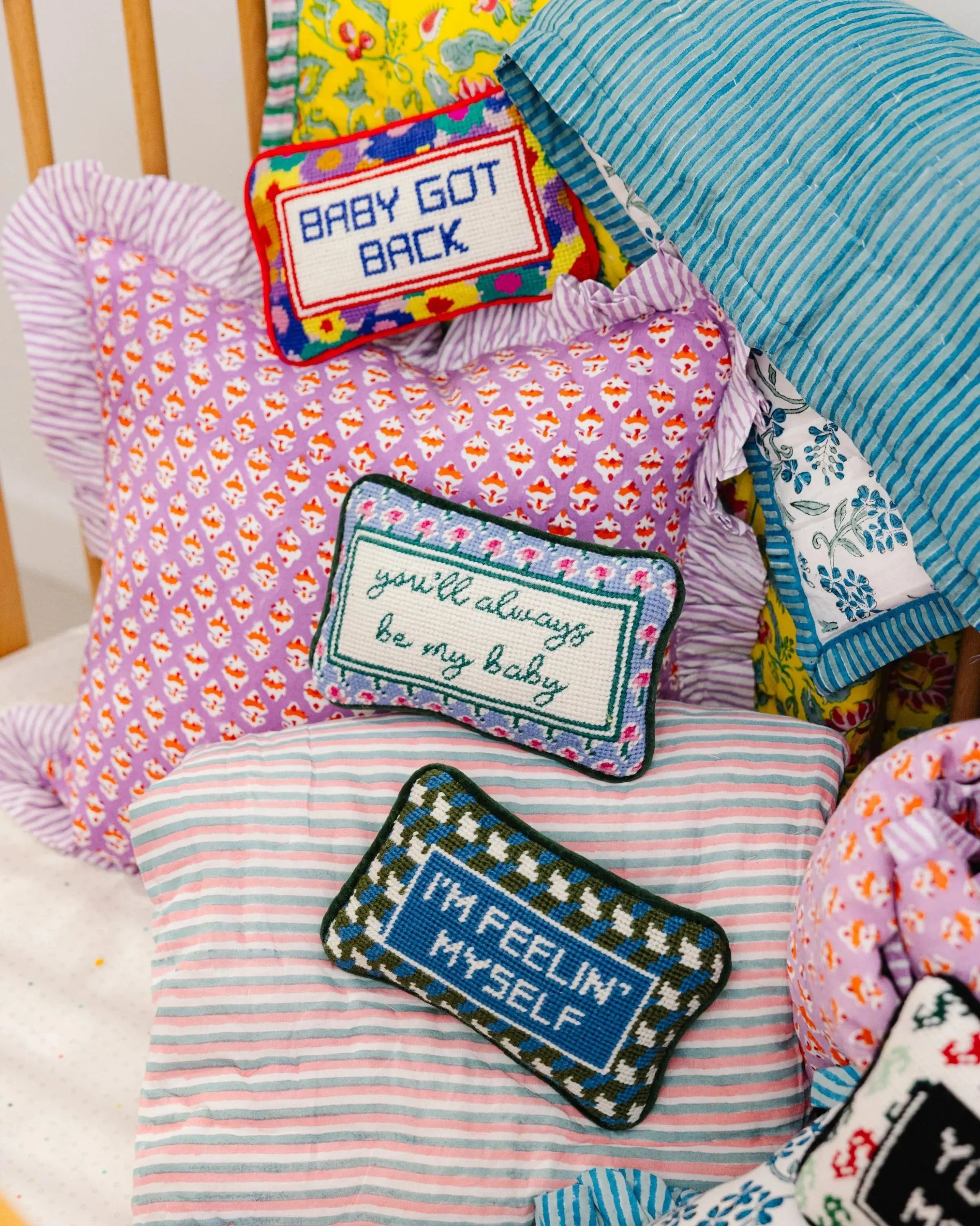 Cozy farmhouse pillows with embroidered phrases like 'Baby Got Back' and 'You'll Always Be My Baby' on floral and striped fabrics.