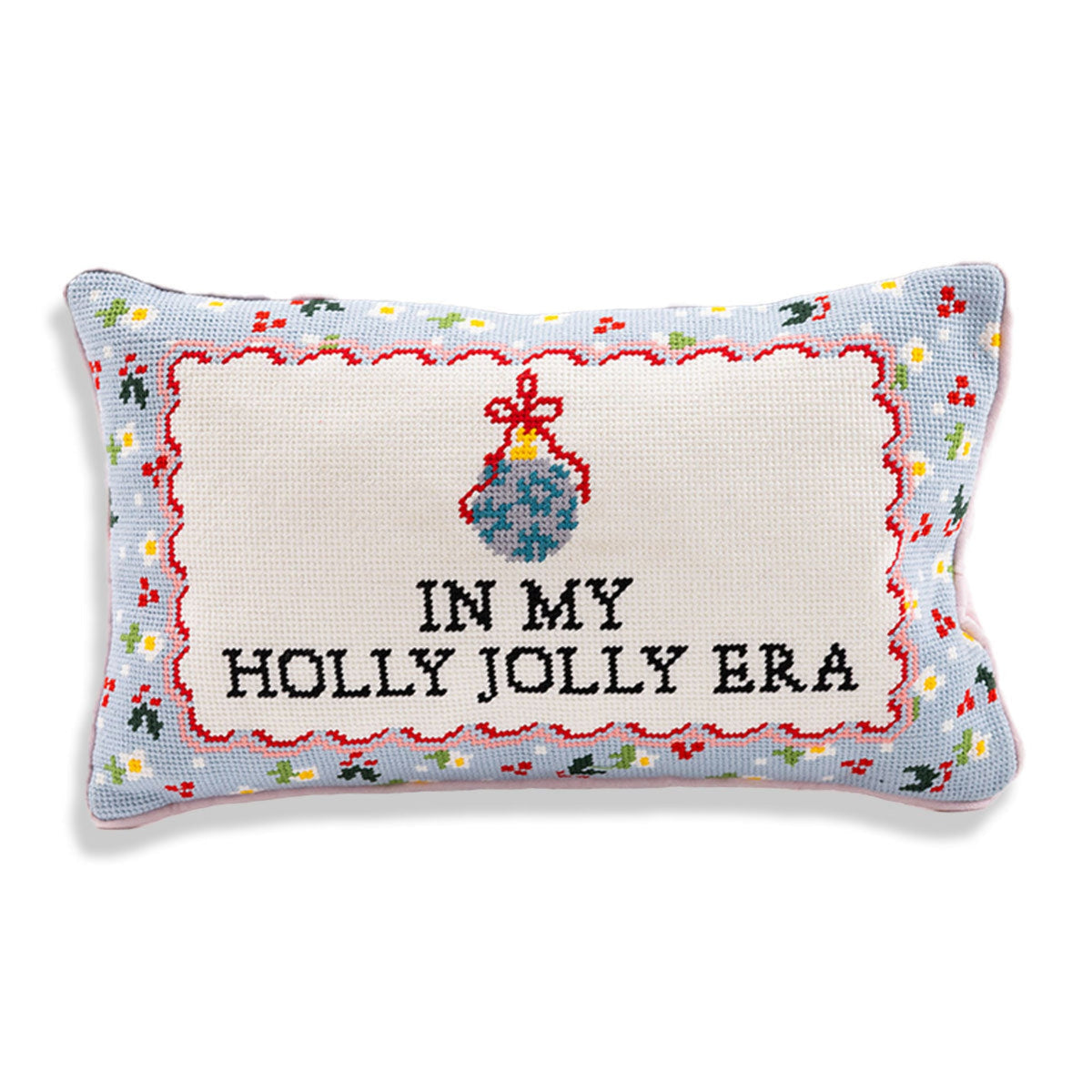 A rectangular cross-stitch cushion with a light blue border and an off-white center panel. The panel features a blue ornament with red and yellow details above the embroidered black text 'IN MY HOLLY JOLLY ERA'.