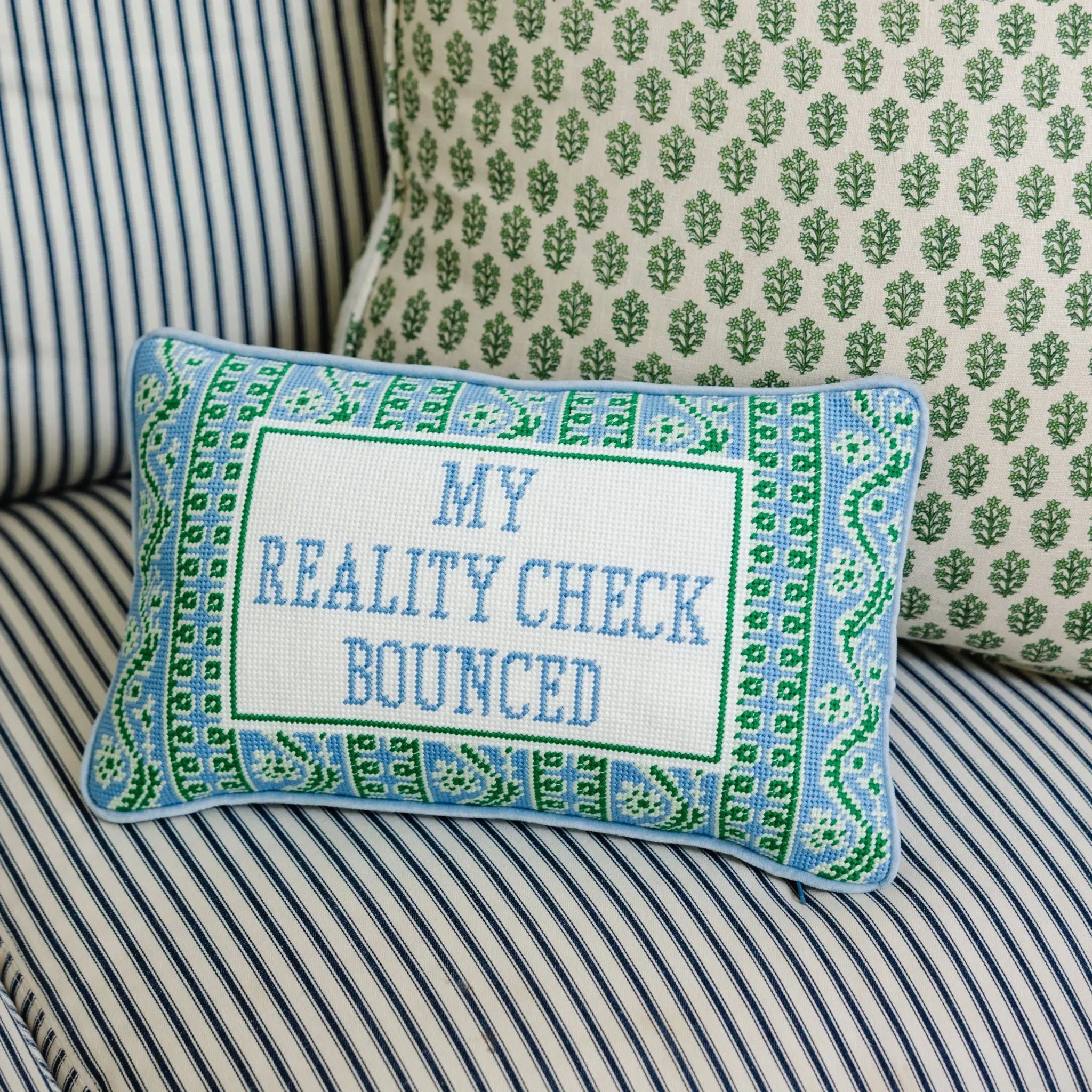 Decorative pillow with 'My Reality Check Bounced' text on a striped sofa.