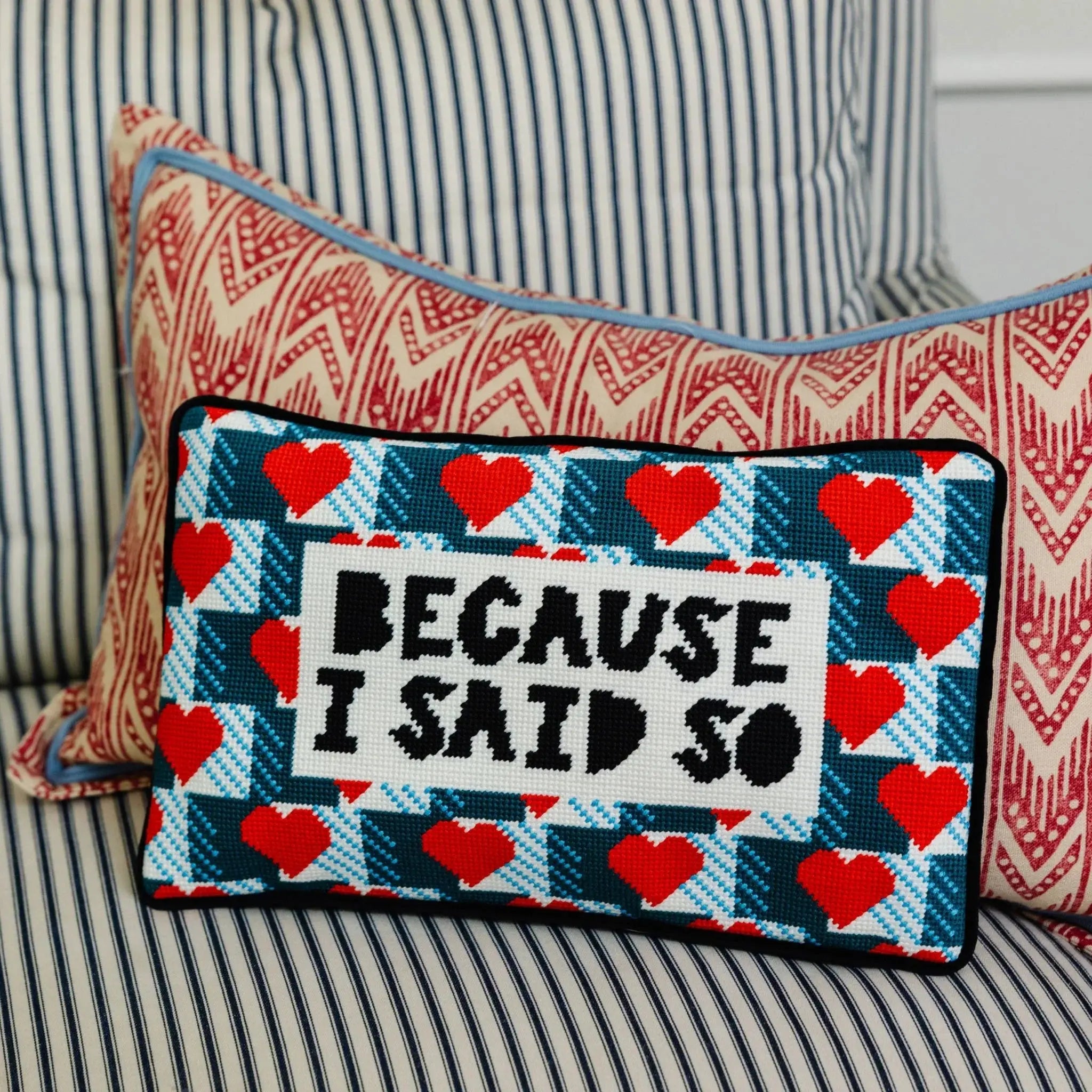 Decorative pillow with heart pattern and text 'Because I said so' on a striped sofa.