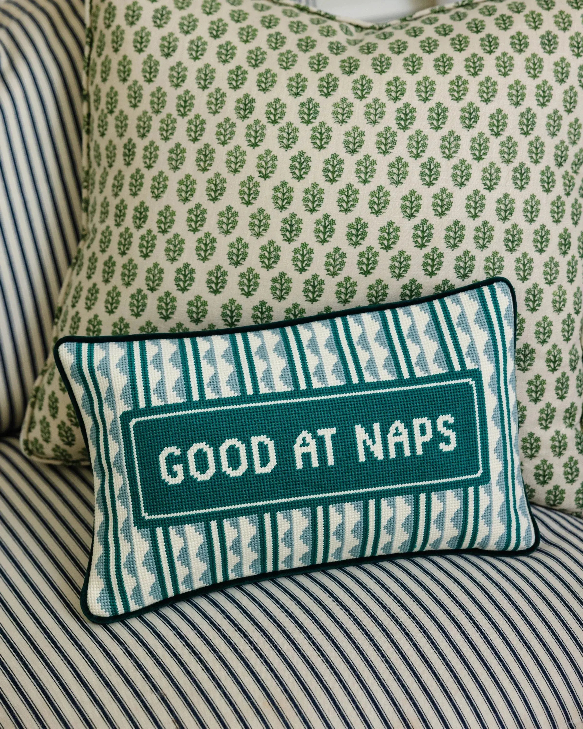 Decorative pillow with 'Good at Naps' text on a striped sofa
