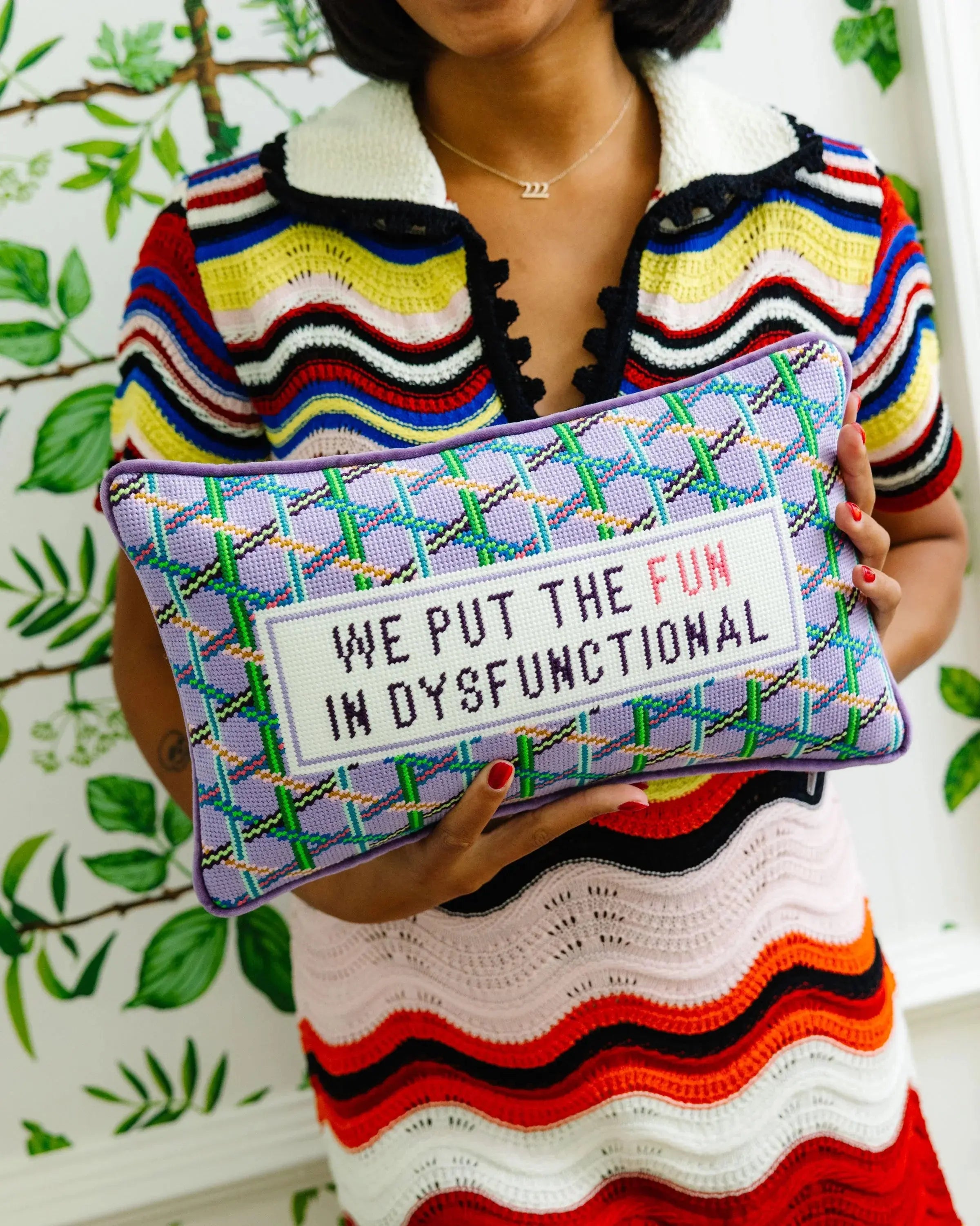 Person holding a colorful pillow with text against a leafy background