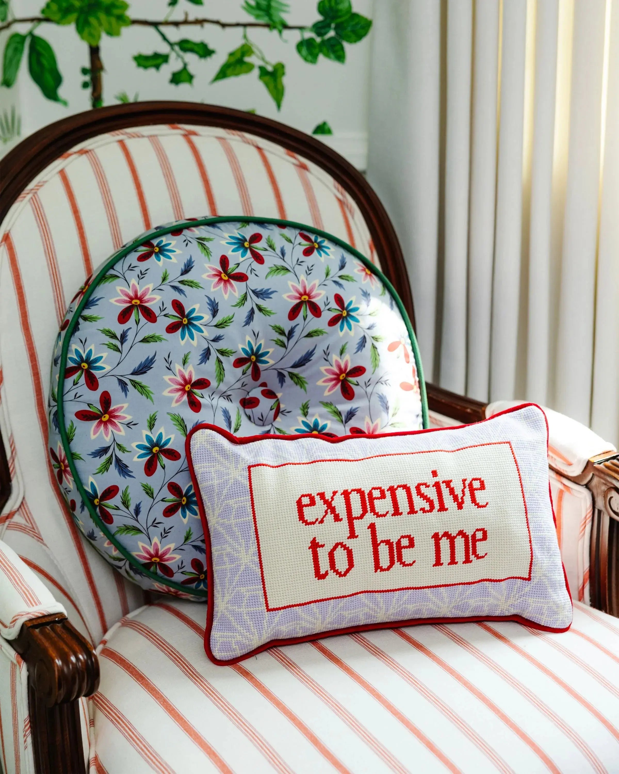Decorative pillow with 'expensive to be me' text on a striped chair with floral cushion