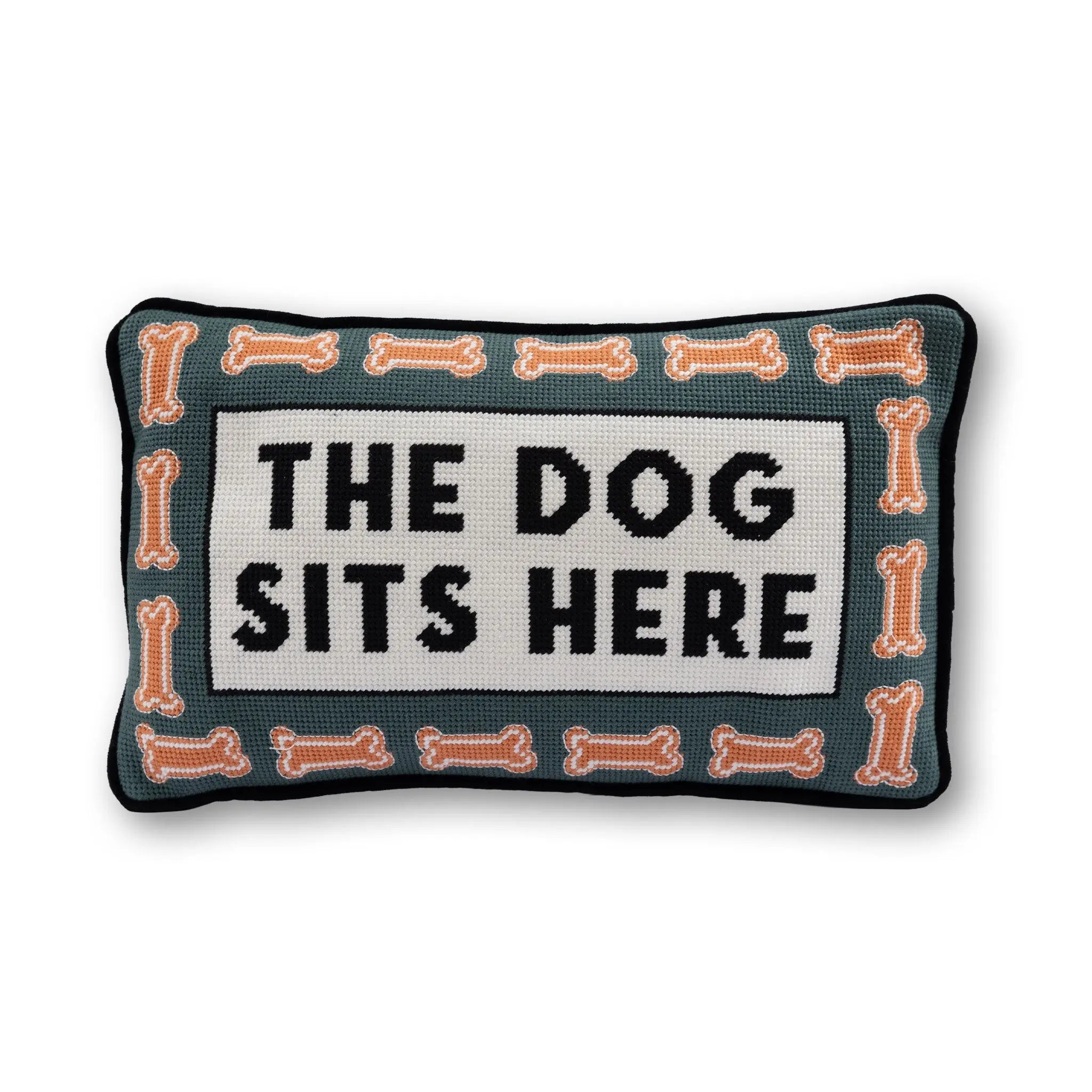 Decorative pillow with 'The Dog Sits Here' text and bone patterns on a white background