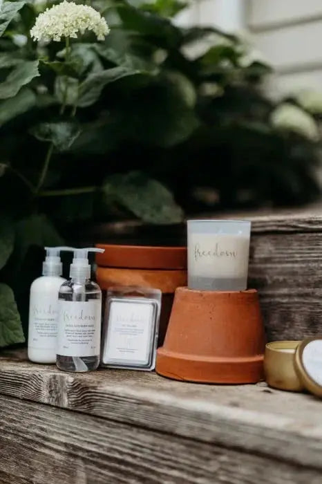 Cozy farmhouse bath essentials and candle with 'freedom' label on rustic wood, greenery backdrop