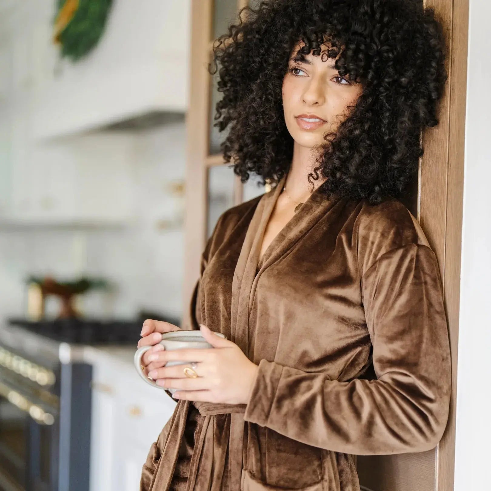 Woman in cozy brown velvet robe holding mug, farmhouse kitchen backdrop, warm home decor vibe