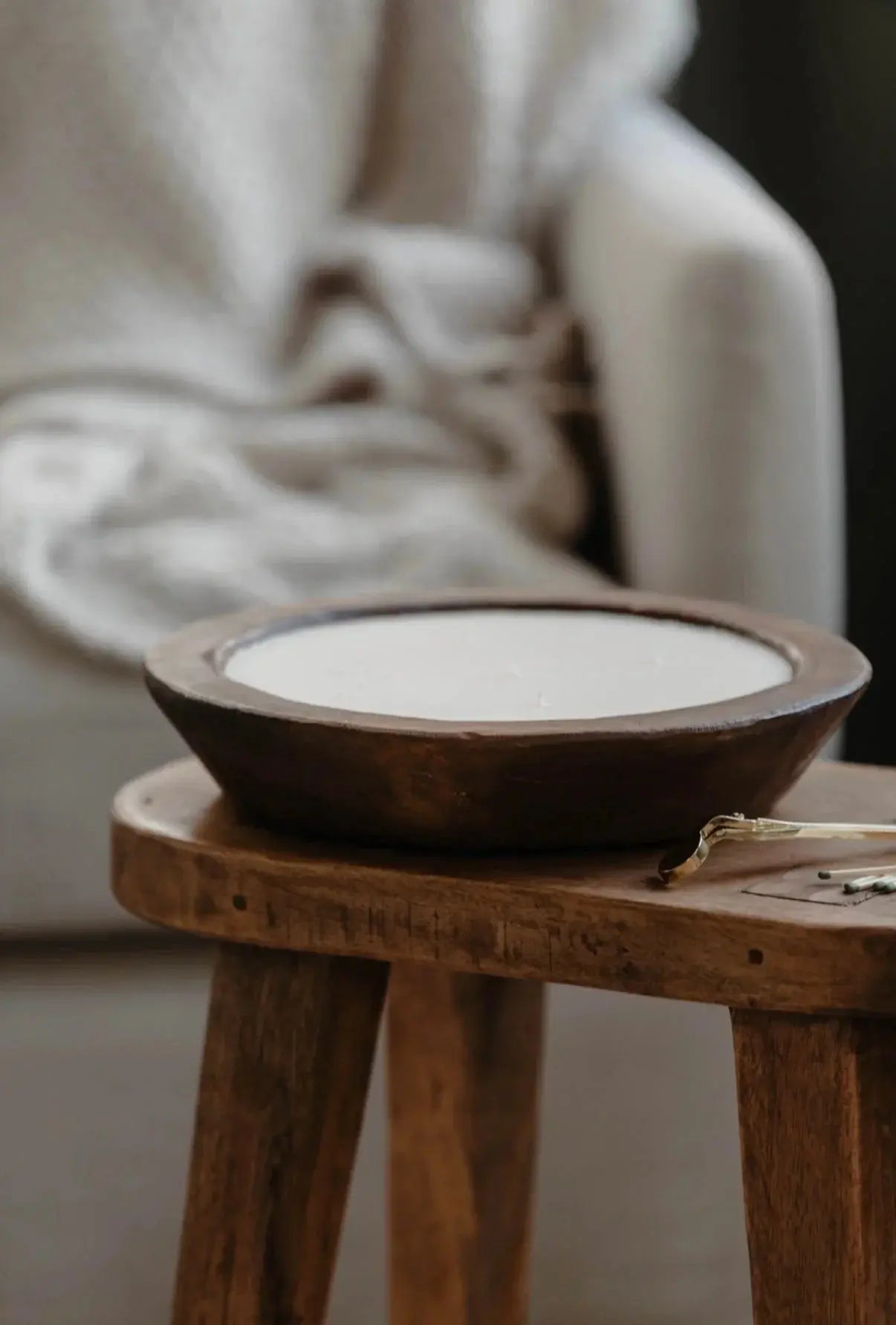 Rustic wooden bowl candle on farmhouse stool with cozy blanket background, perfect for cottage home decor