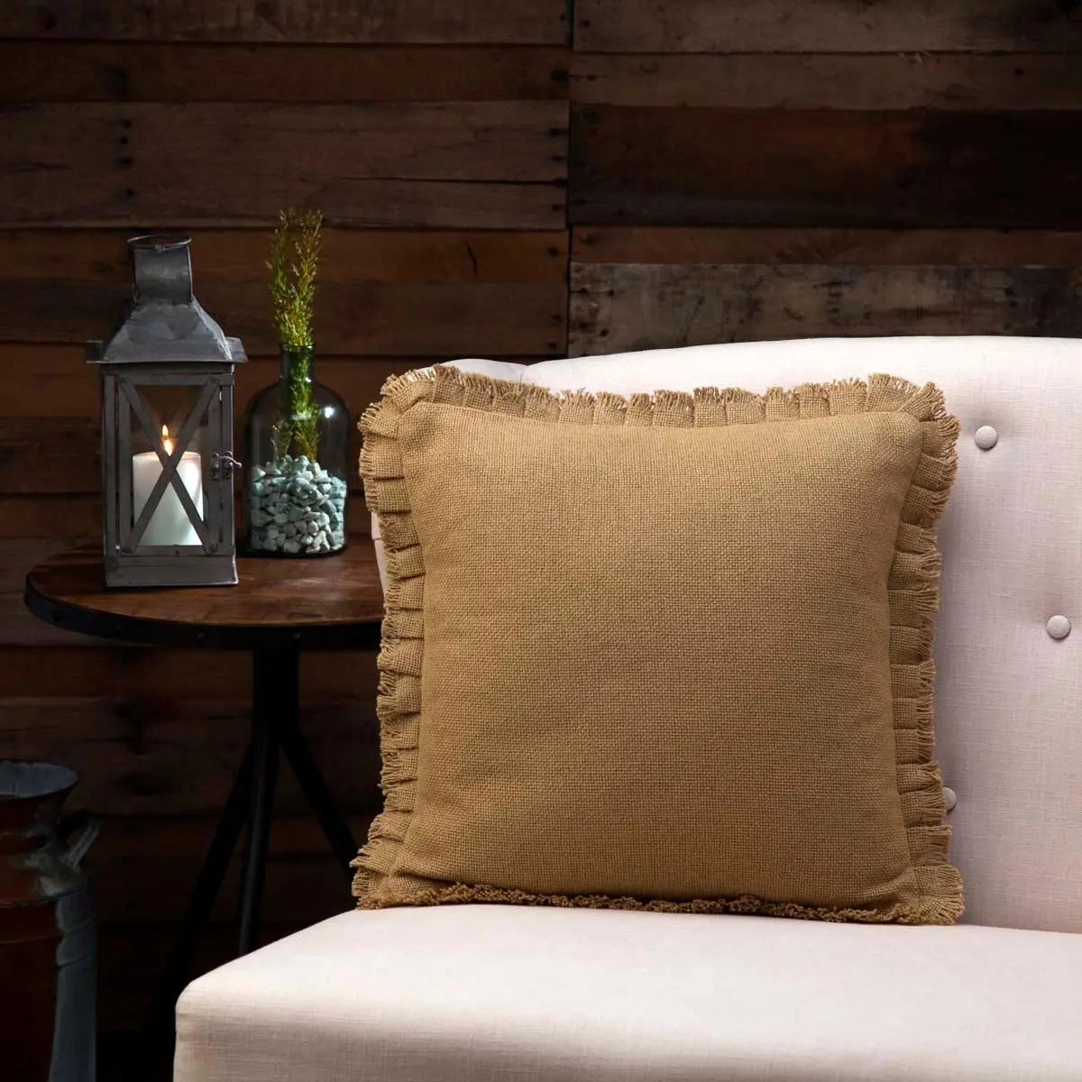 Rustic burlap throw pillow with fringe on cozy farmhouse chair, lantern and greenery decor