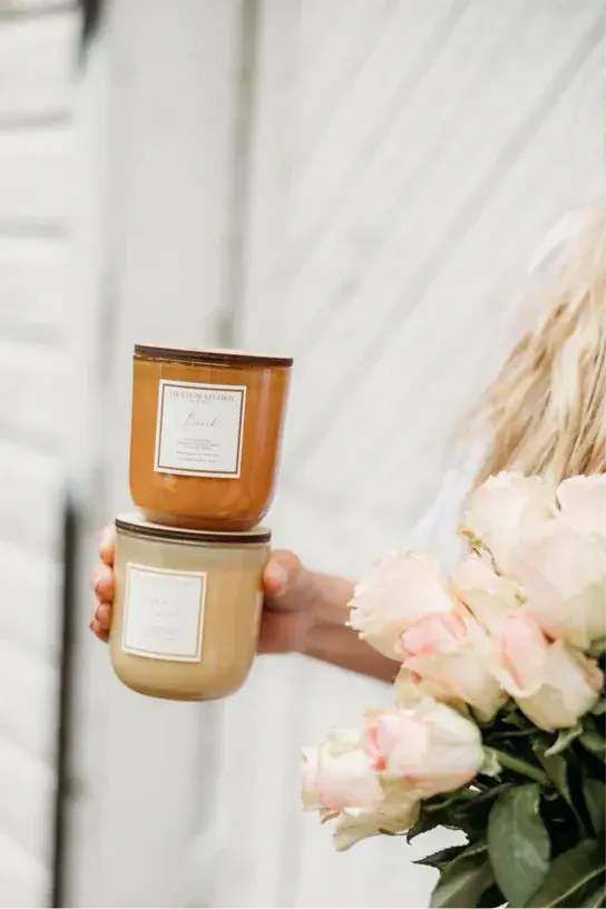 Cozy farmhouse-style candles with soft labels, held beside blush roses for warm home decor