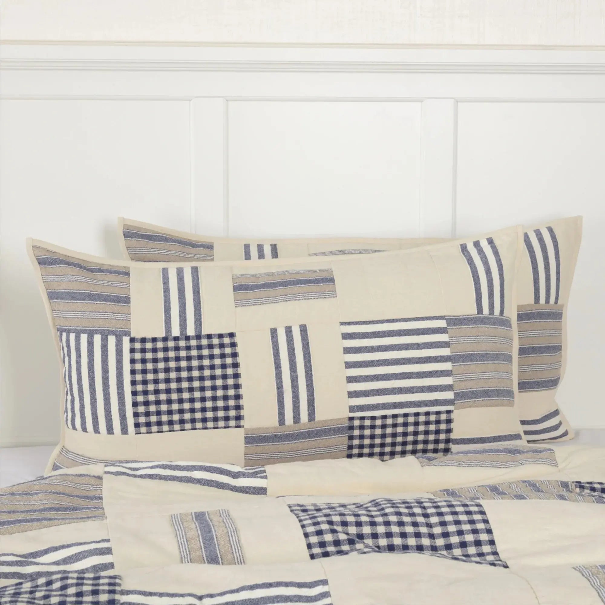 Farmhouse patchwork quilt set with blue, white, and beige stripes and gingham squares on a cozy bed