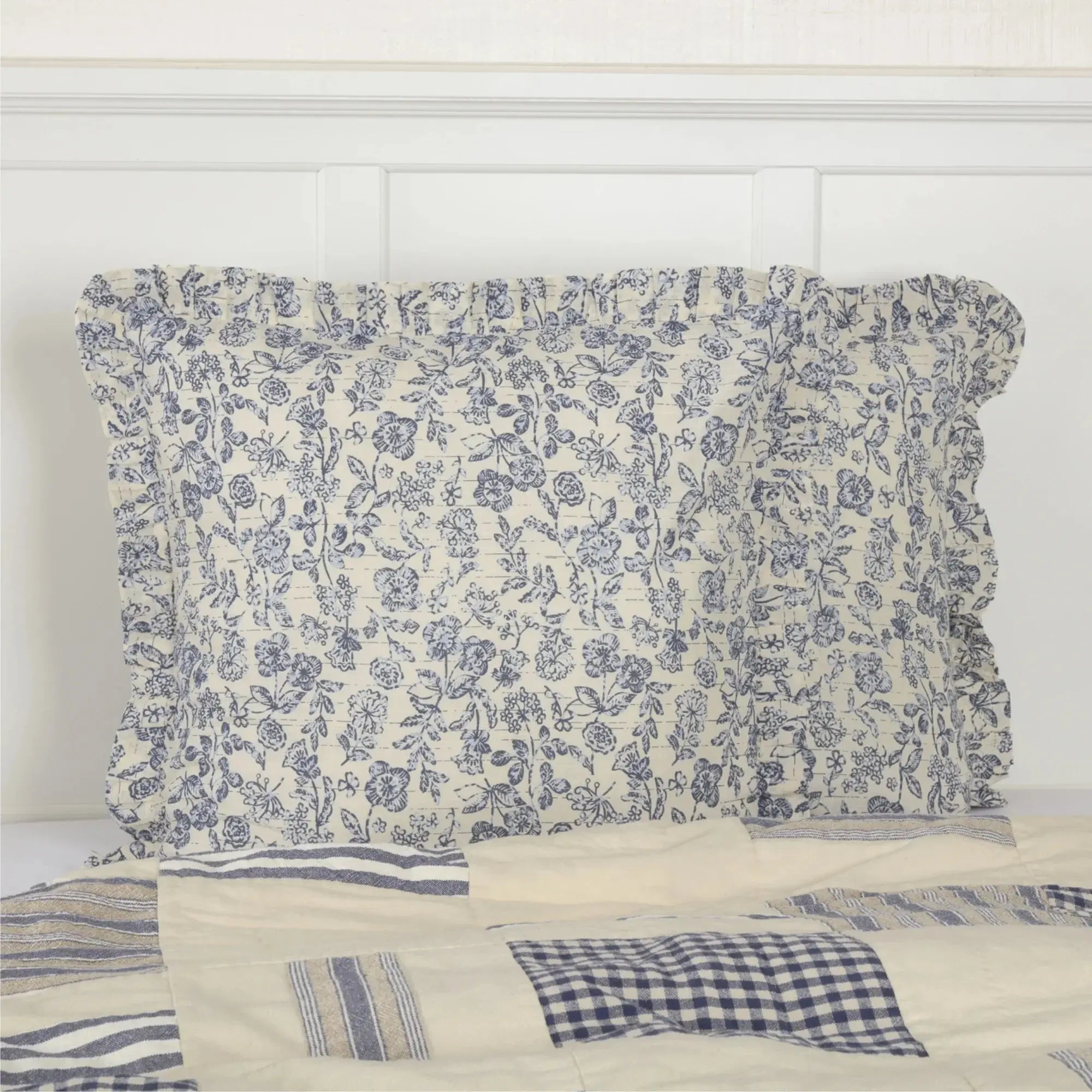 Blue floral ruffled pillowcase on farmhouse-style bed with patchwork quilt, cozy cottage decor