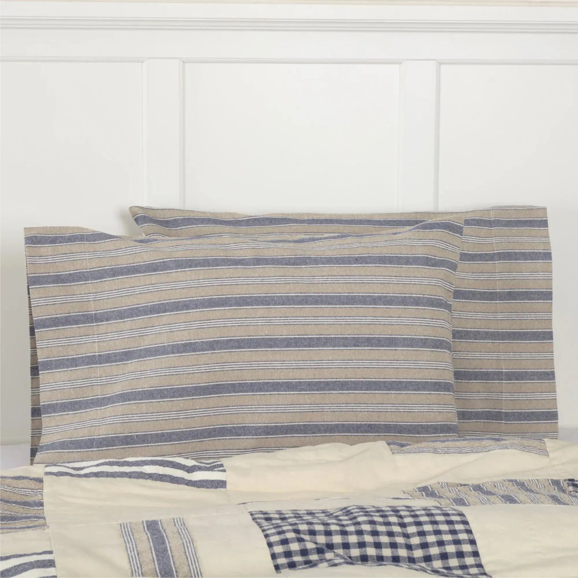 Blue and beige striped farmhouse pillowcases on white bed with patchwork quilt, cozy cottage bedroom decor