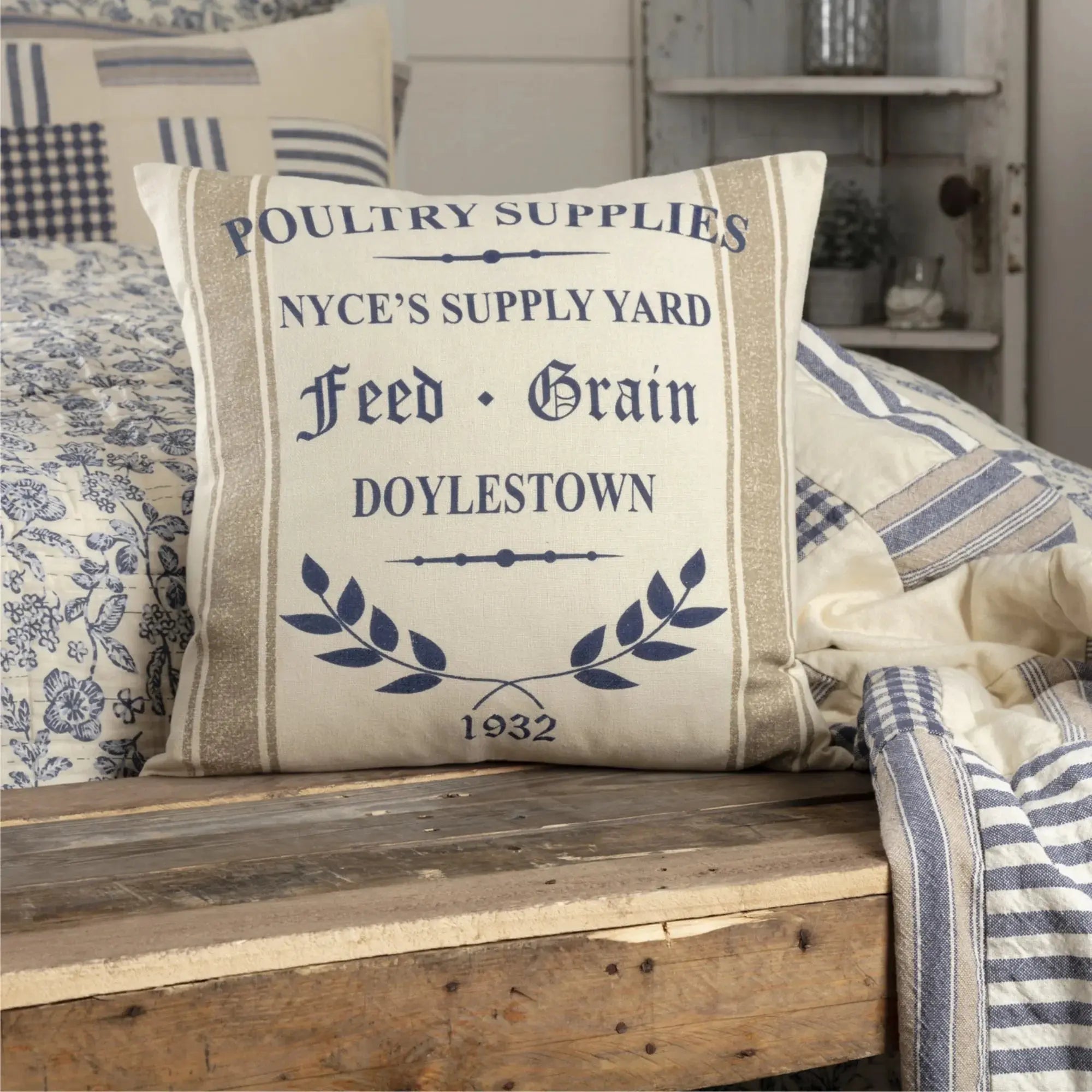 Farmhouse pillow with 'Poultry Supplies' text, blue laurel wreath, and 1932 design on rustic wood bench