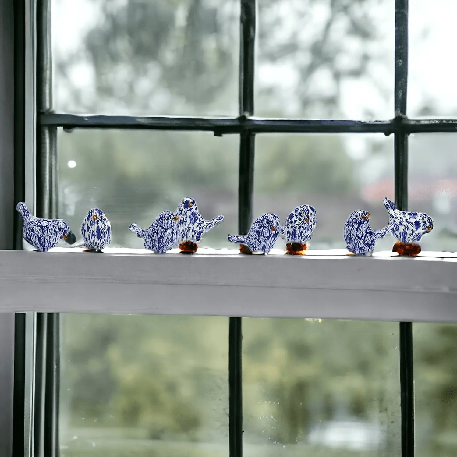 Decorative blue and white ceramic birds on a windowsill with a blurred outdoor background