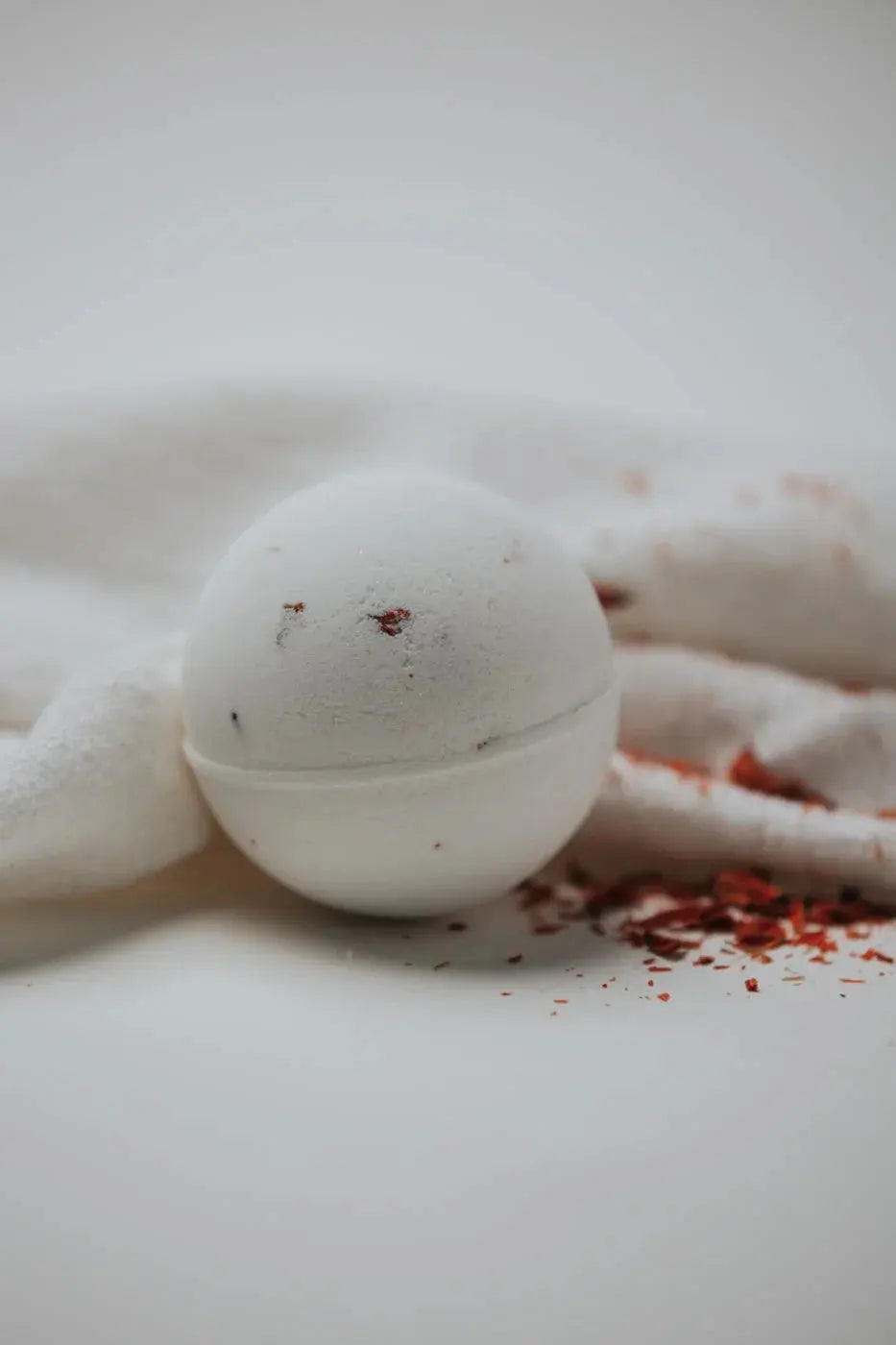 White bath bomb with red botanical specks on soft towel, cozy bath essentials for relaxation