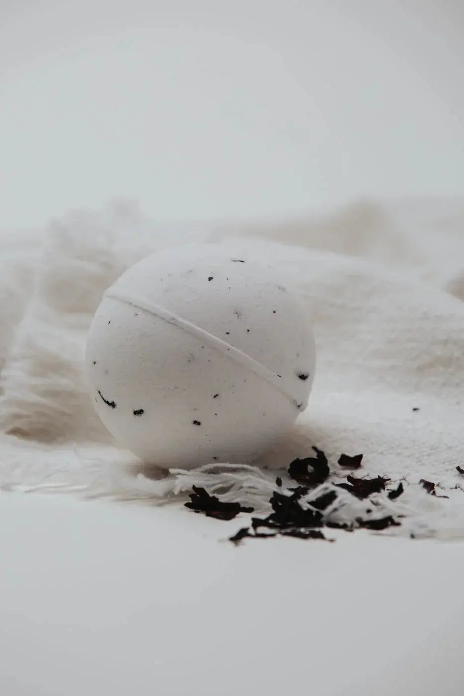 White bath bomb with black speckles on cozy white towel, perfect for relaxing self-care routines