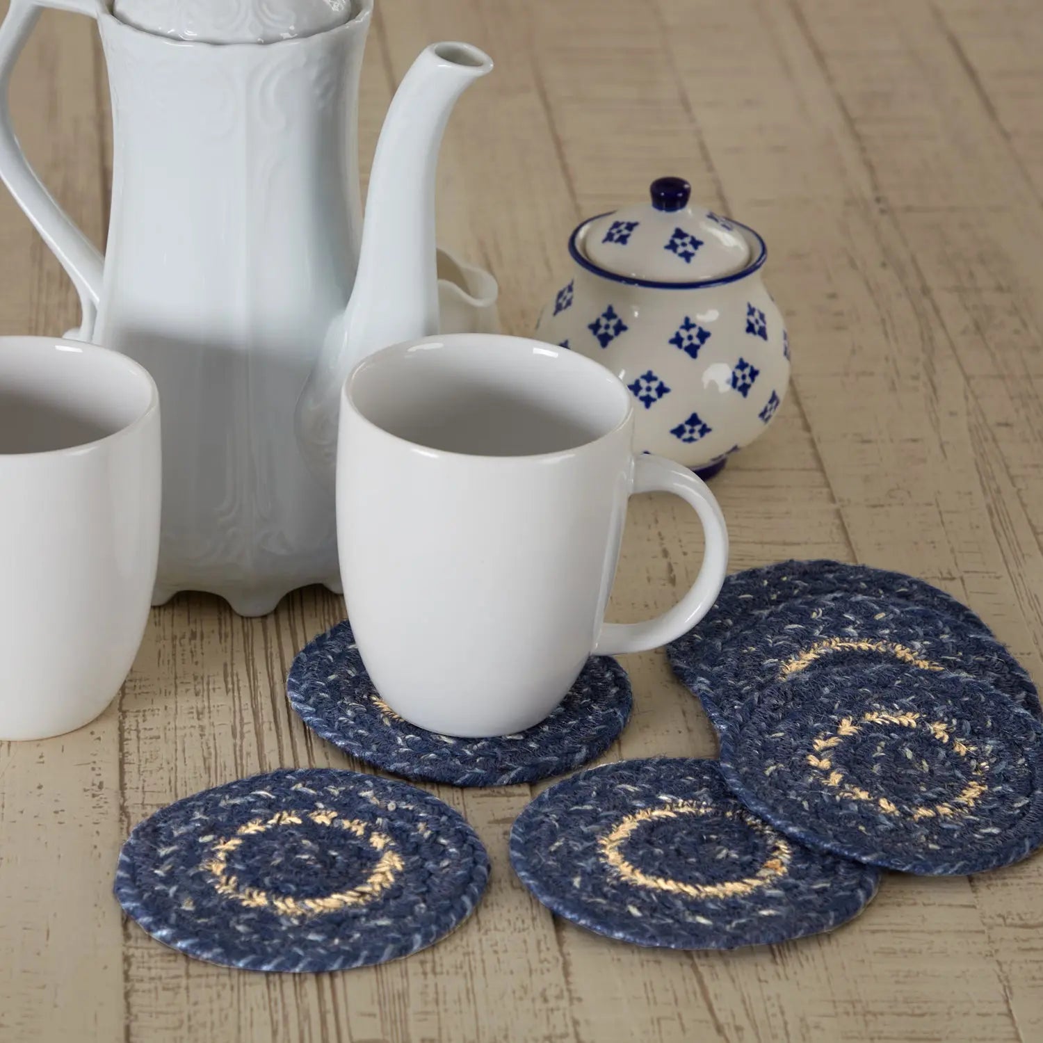 White teapot, mug, and decorative blue coasters on a wooden surface
