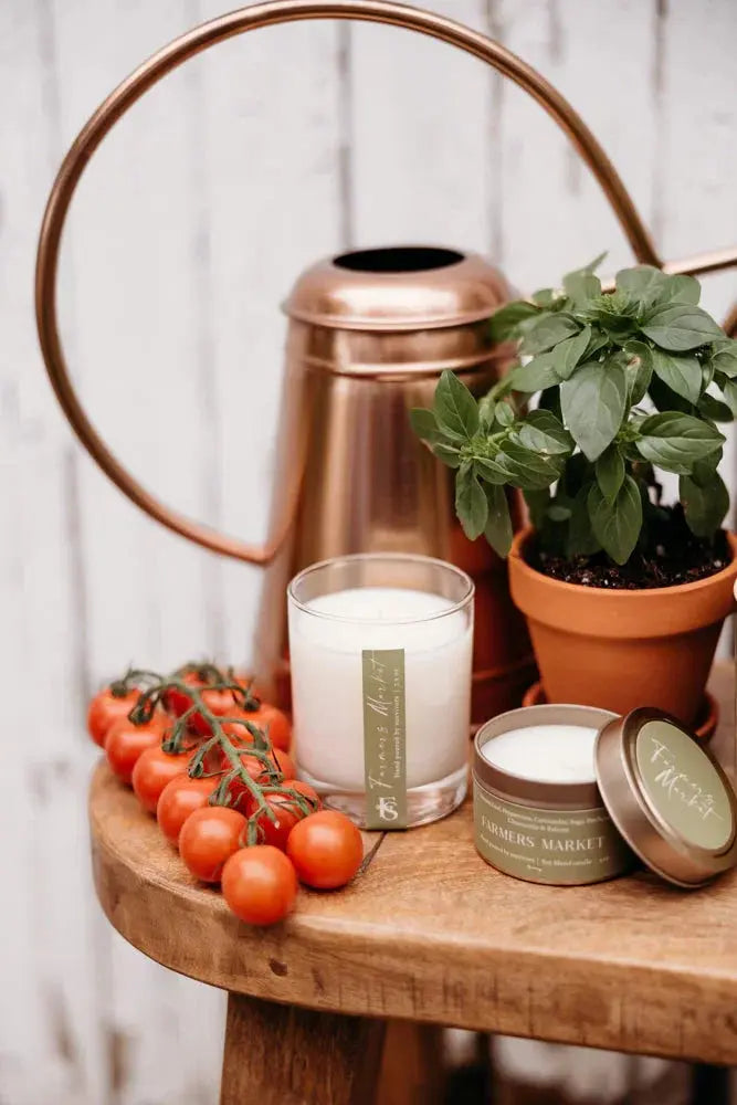 Farmers Market scented candle, basil plant, cherry tomatoes, and copper watering can on rustic wood table