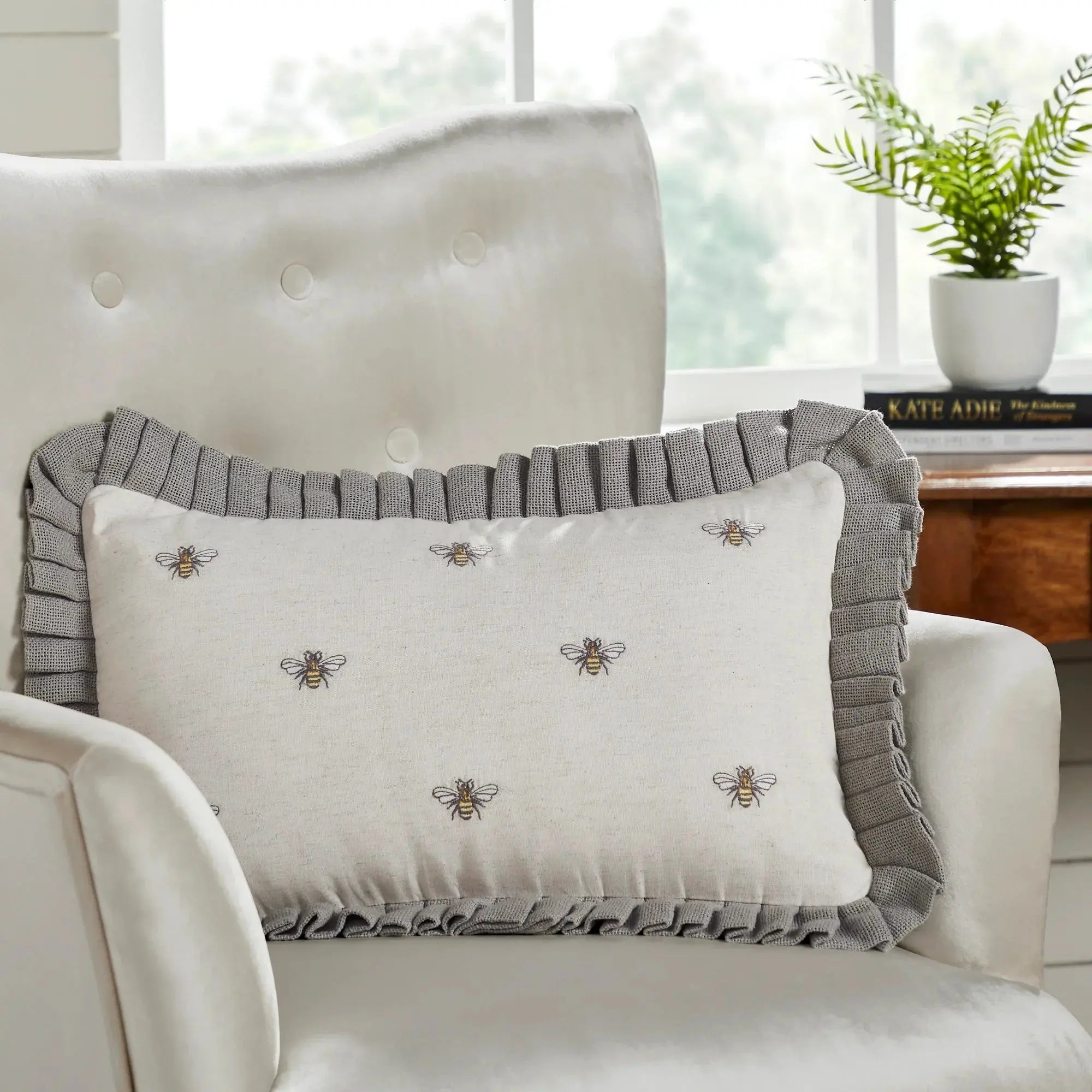 Beige pillow with embroidered bees and gray ruffle trim on cozy armchair, farmhouse decor