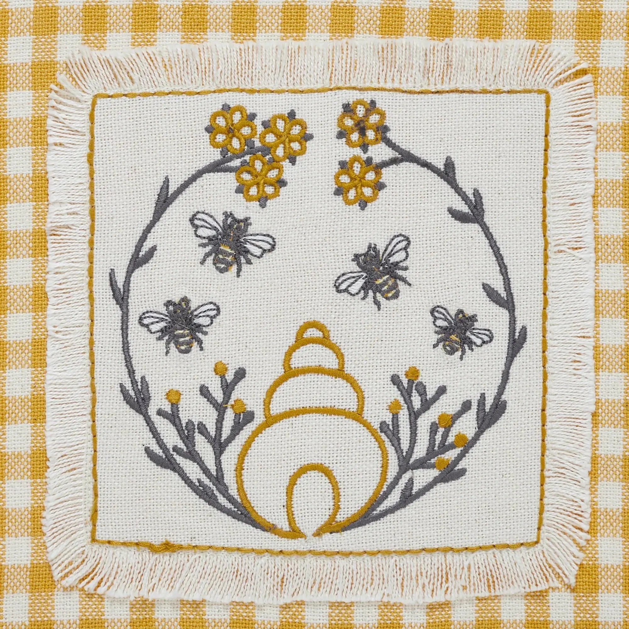 Embroidered bee and beehive pillow with yellow flowers on farmhouse-style gingham background