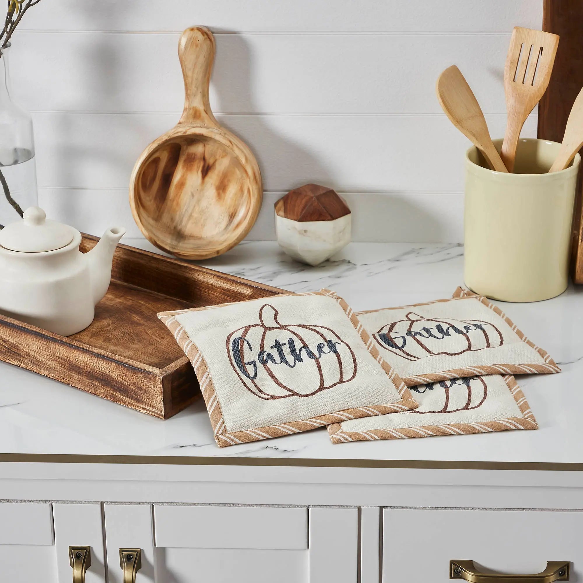 Kitchen counter with wooden utensils, a teapot, and decorative coasters with pumpkin designs.