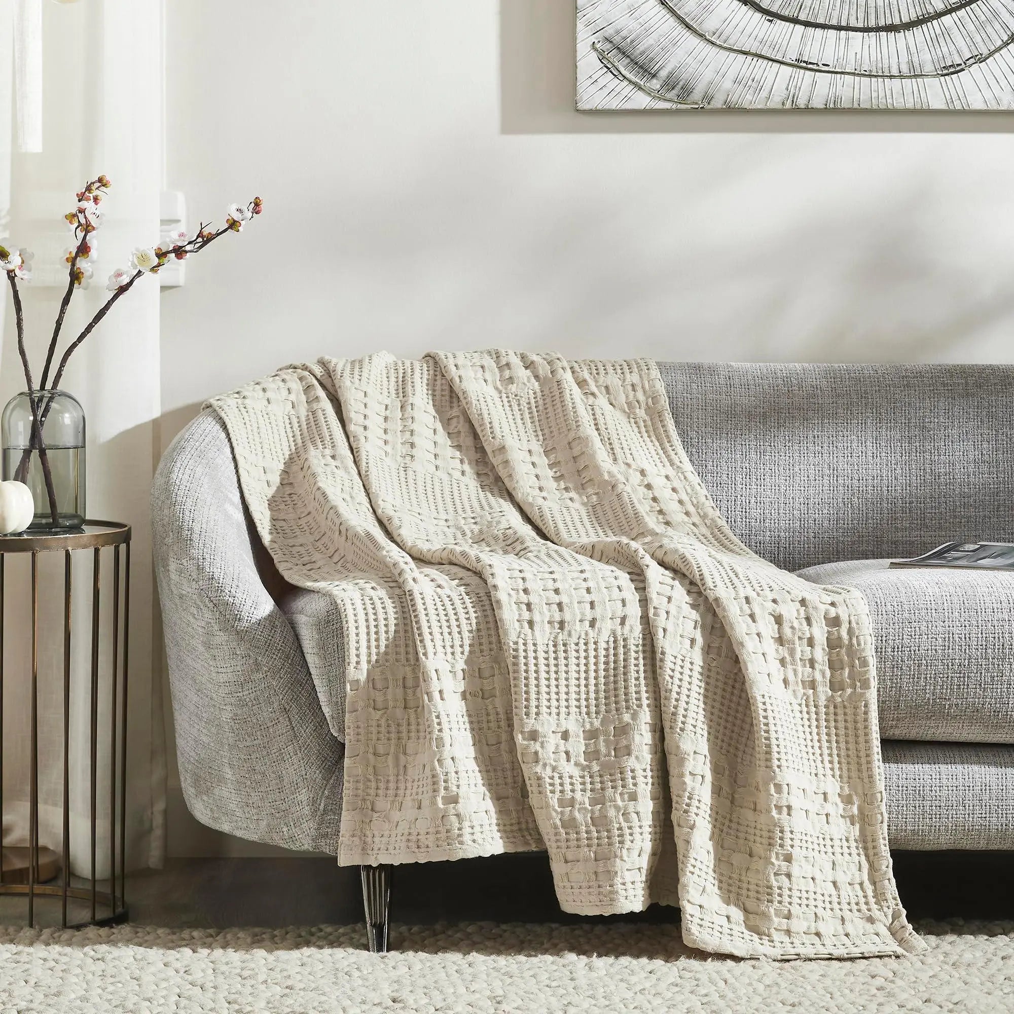 Cream textured throw blanket on gray sofa, cozy farmhouse living room decor with floral vase and wall art