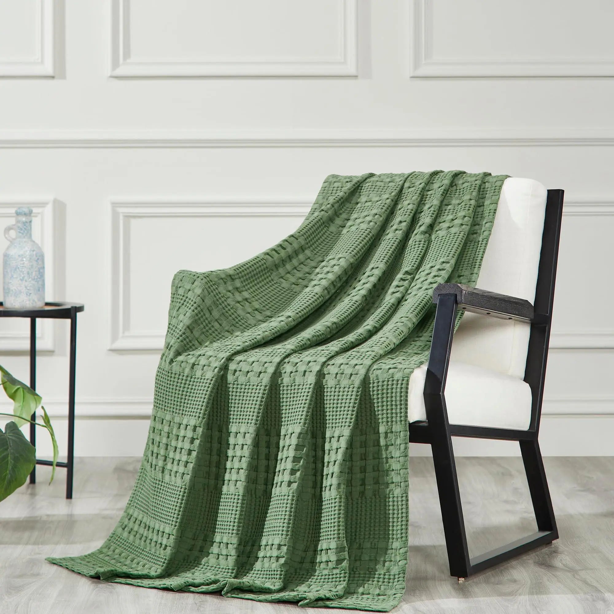 Sage green waffle knit throw blanket draped over modern armchair, cozy farmhouse decor