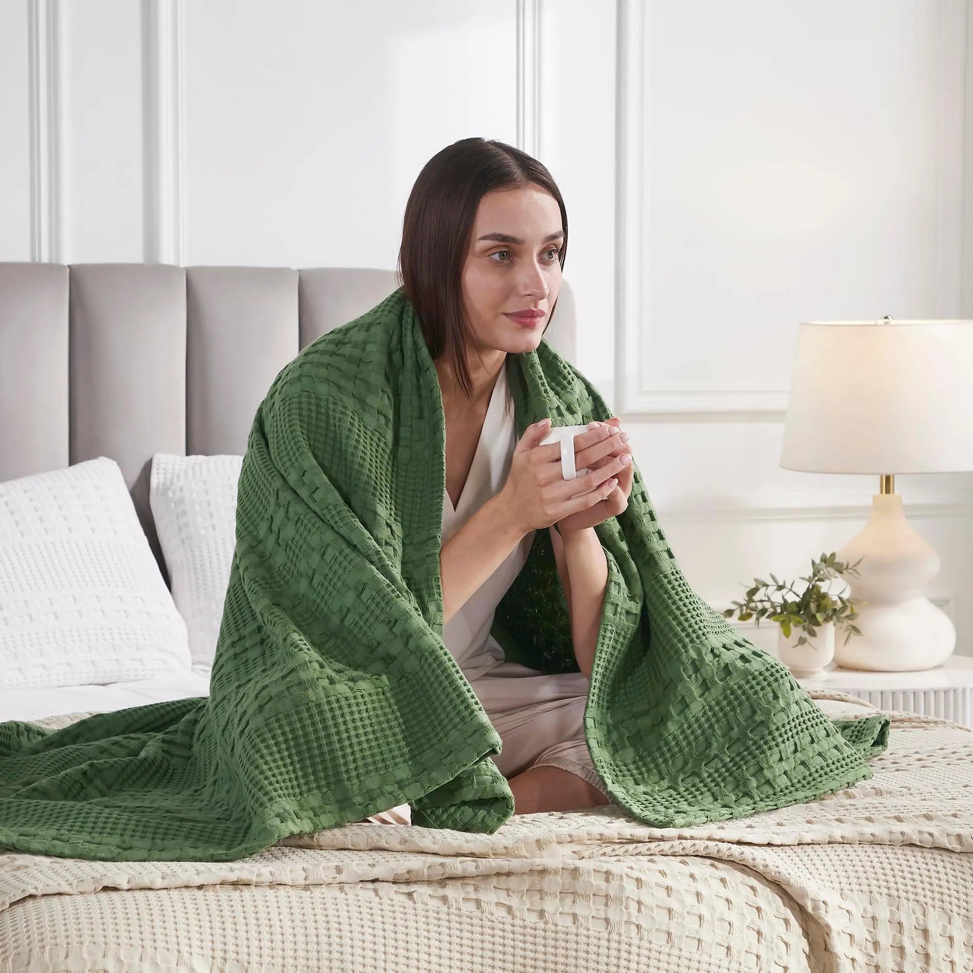 Woman wrapped in cozy green waffle knit blanket on bed, holding mug, farmhouse decor style