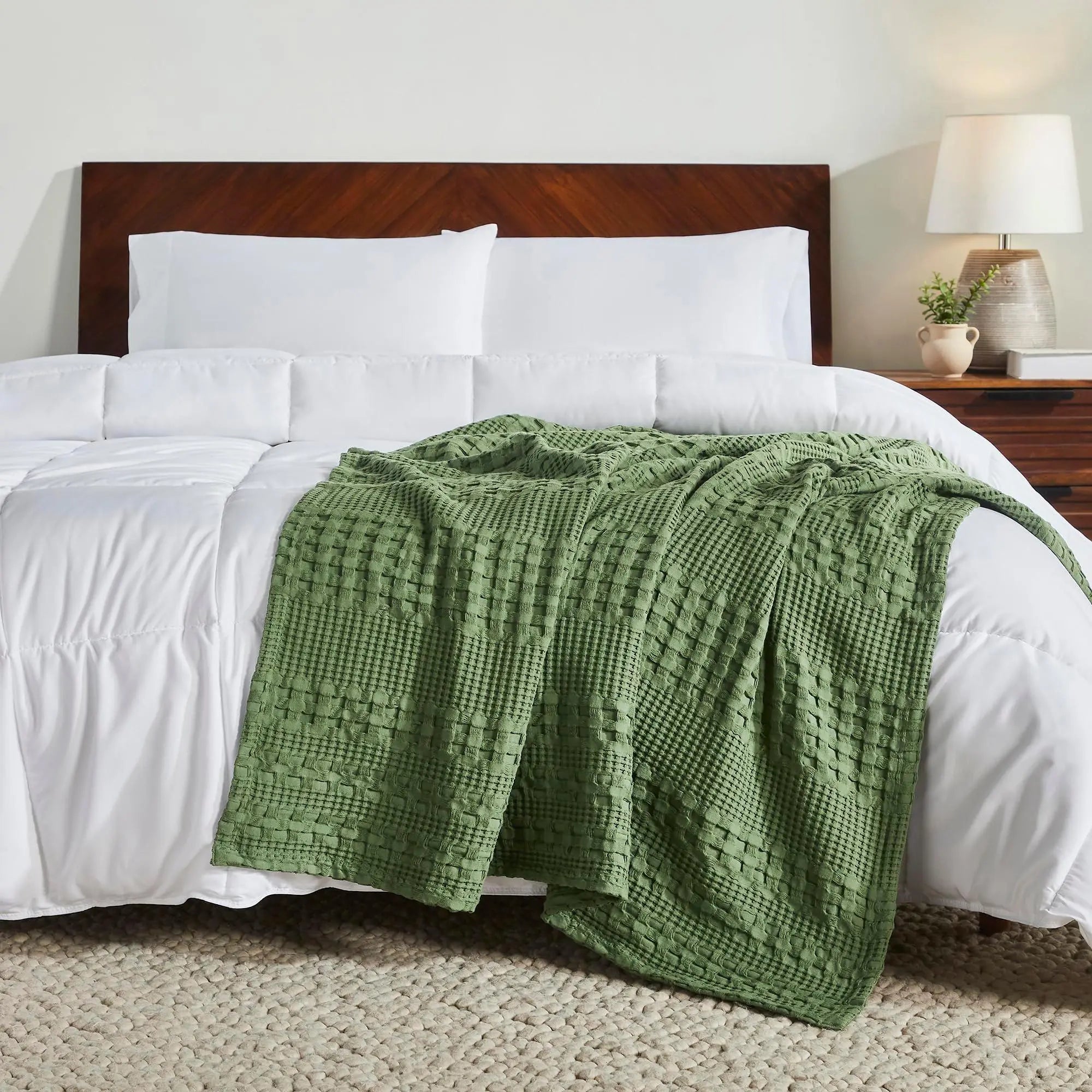 Green waffle knit throw blanket on cozy farmhouse bed with white linens and wooden headboard