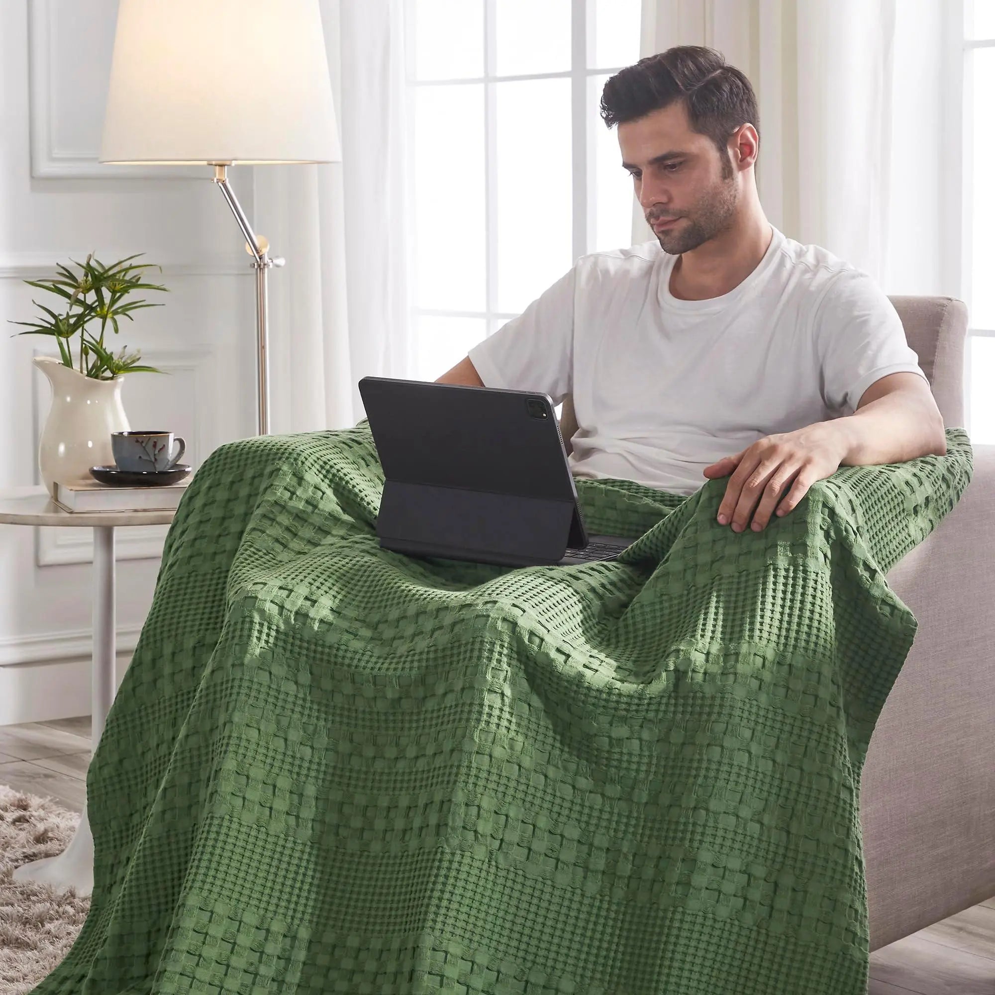 Man relaxing under cozy green waffle knit blanket while using tablet in farmhouse-style living room