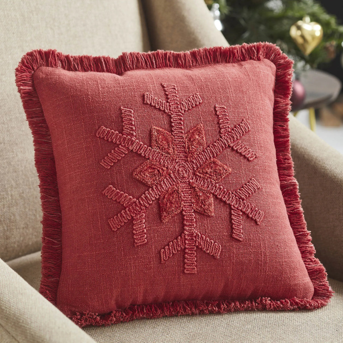 Red textured pillow with embroidered design on a beige couch