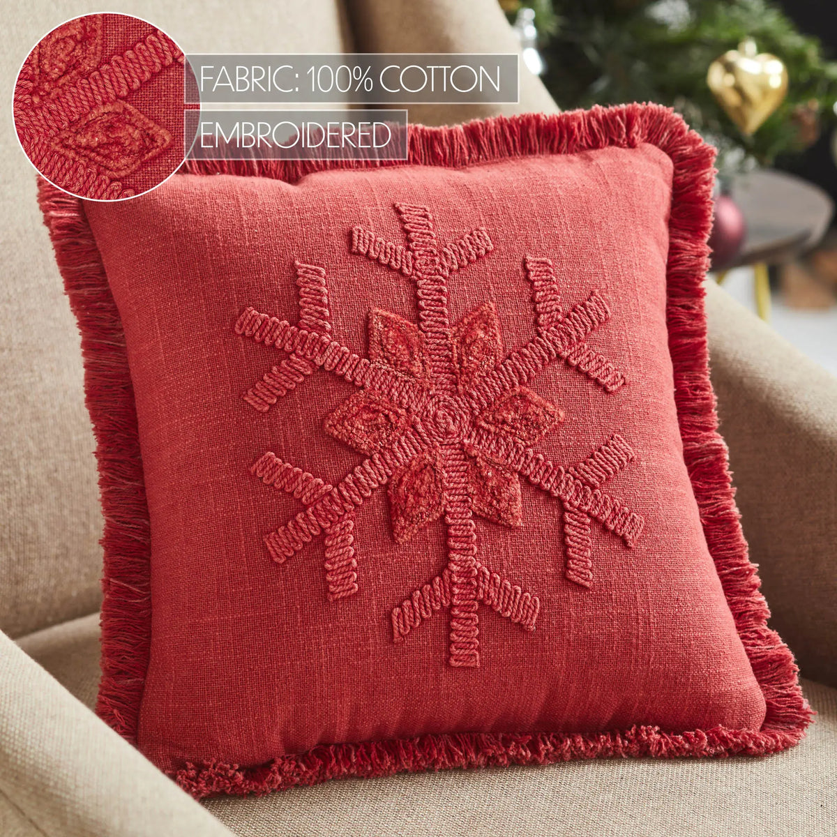 Red embroidered pillow on a beige couch with fabric and embroidery details.