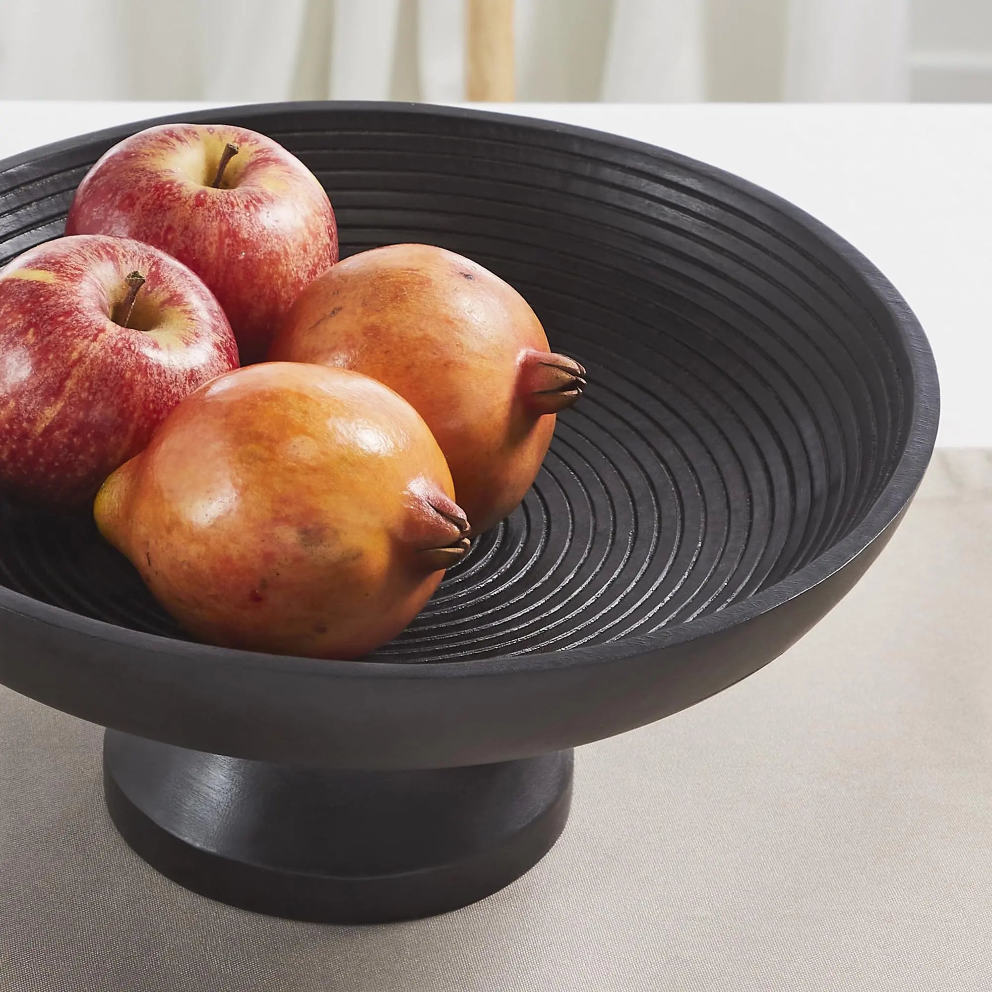 Black textured bowl with apples and pomegranates on a light background