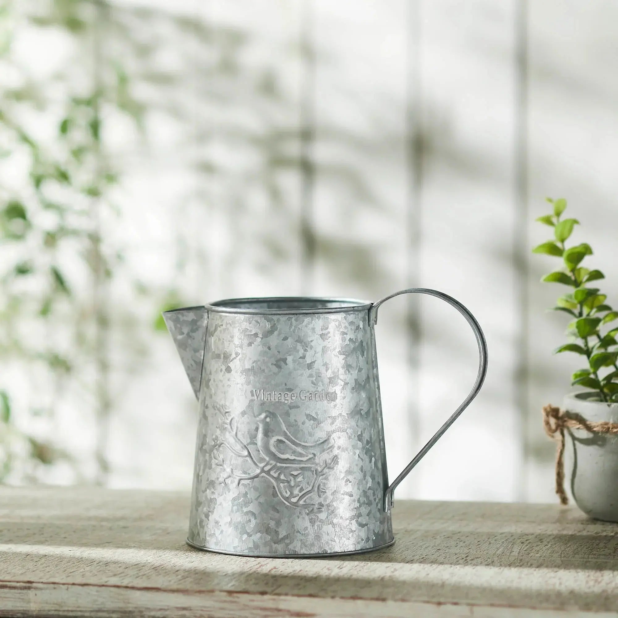 Metal watering can on a wooden surface with a blurred natural background